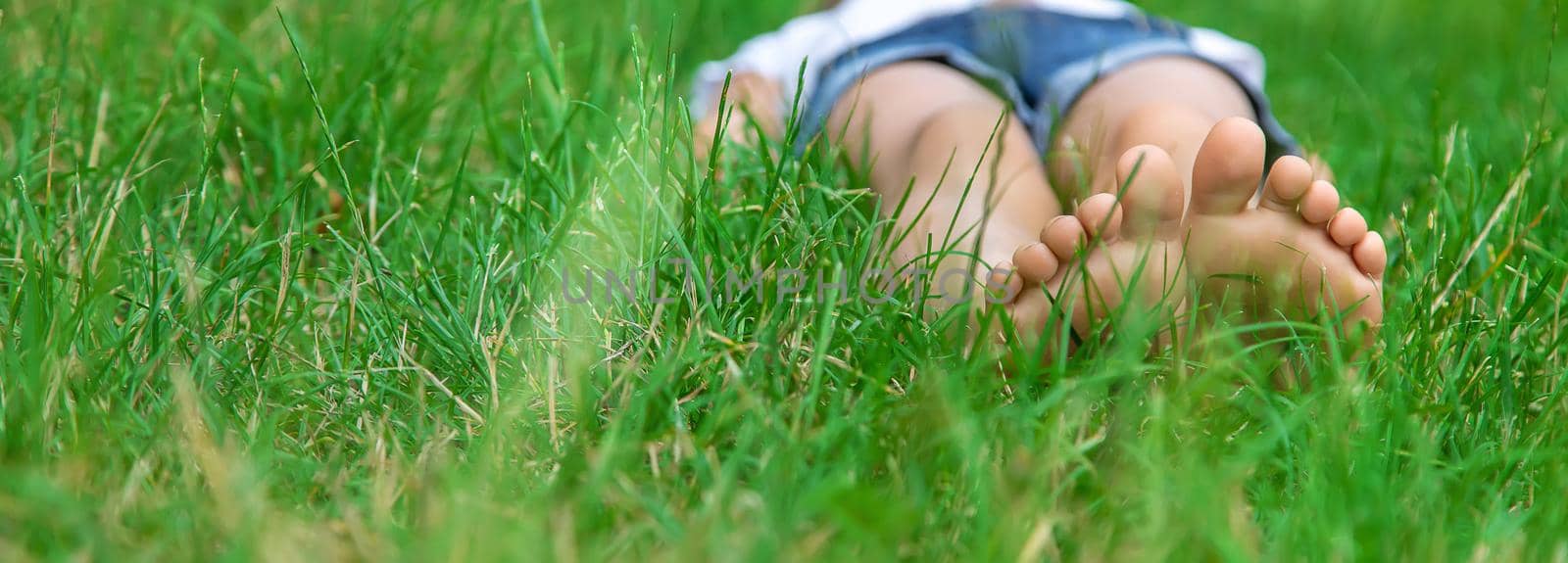 Children's feet on the green grass in the park. Selective focus. by yanadjana