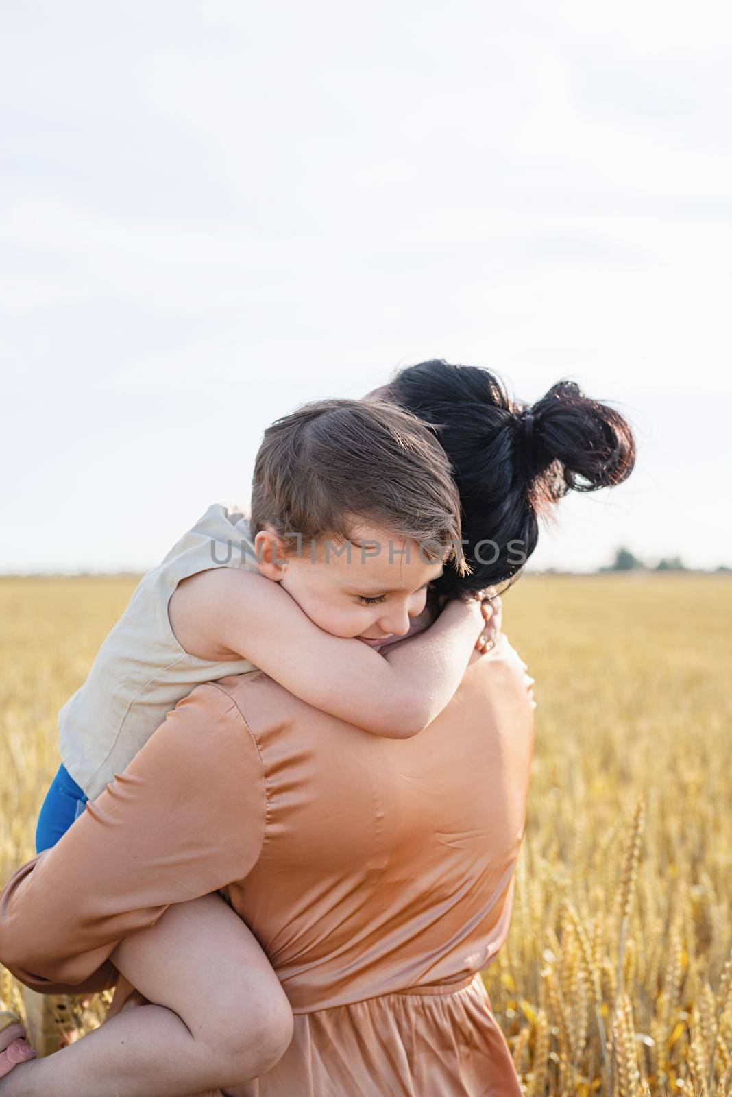 Happy family on a summer walk, mother and child walk in the wheat field and enjoy the beautiful nature, at sunset, hugging and kissing