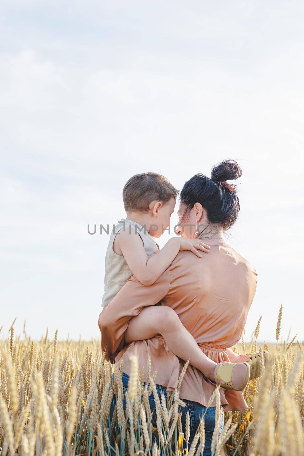 Happy family of mother and infant child walking on wheat field, hugging and kissing by Desperada