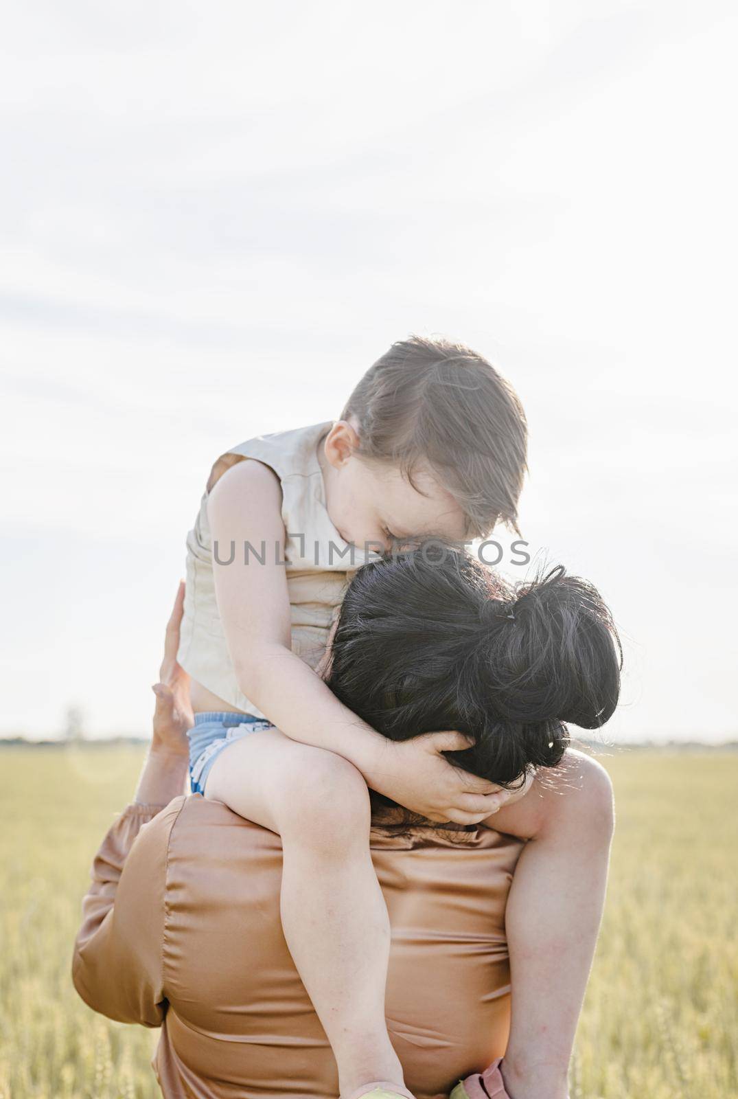 Happy family of mother and infant child walking on wheat field, hugging and kissing by Desperada