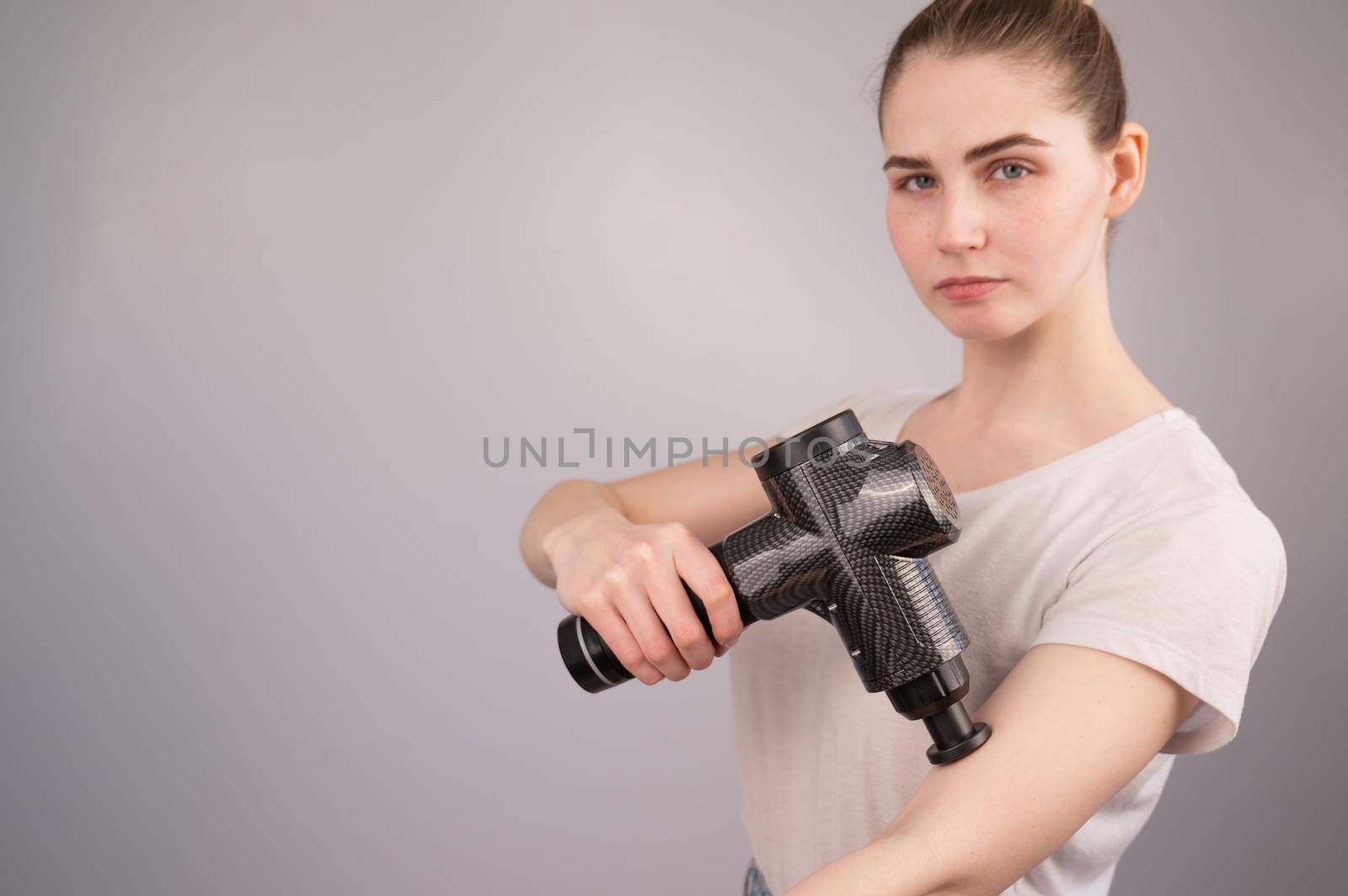 Caucasian woman uses a massager gun for pain in the muscles of the arm