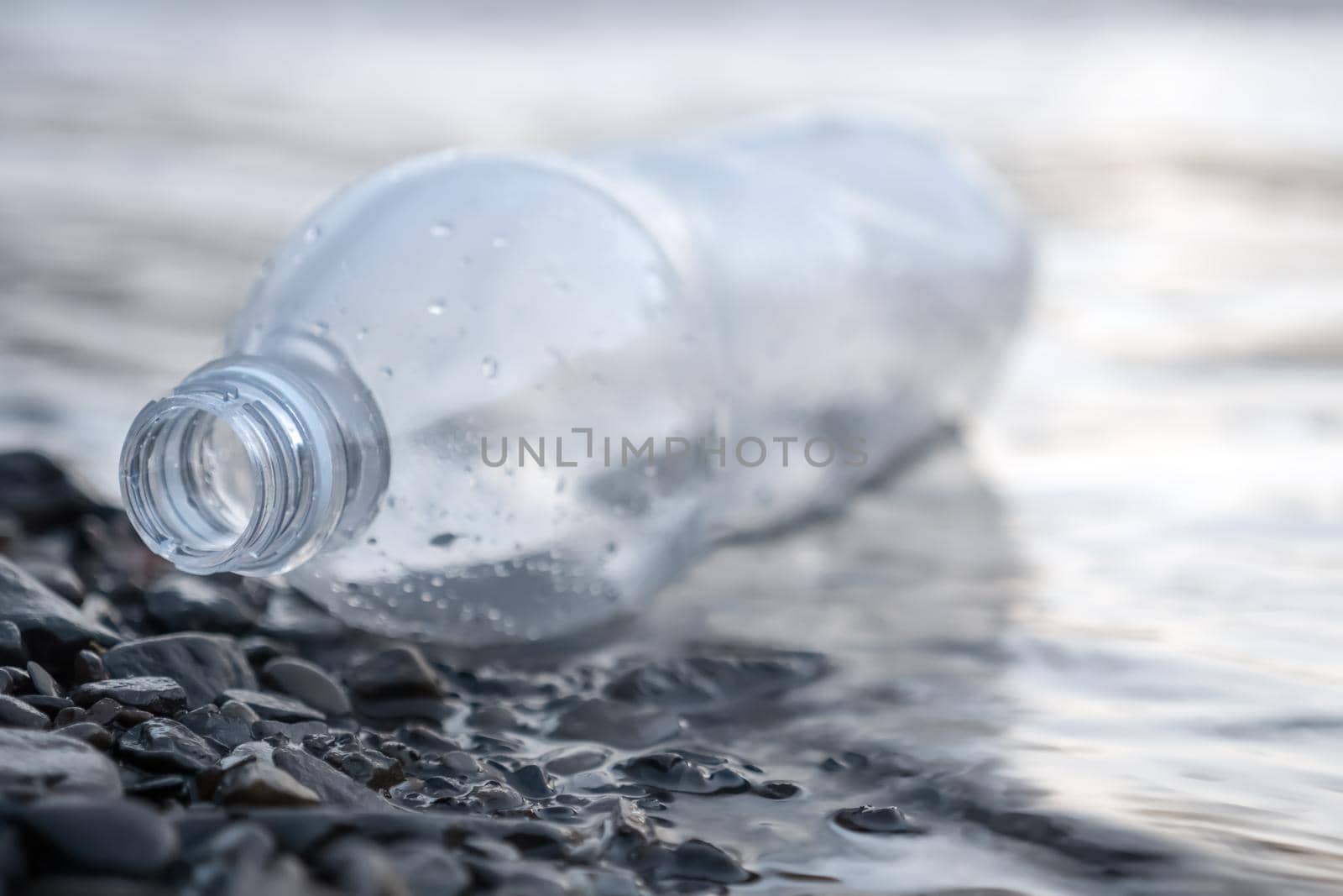 Discarded bottle plastic garbage sea waste. Ecology pollution of nature. Environmental problems. Sea pollution garbage water trash on beach. Empty bottle plastic trash lying on shore sea water waste by synel