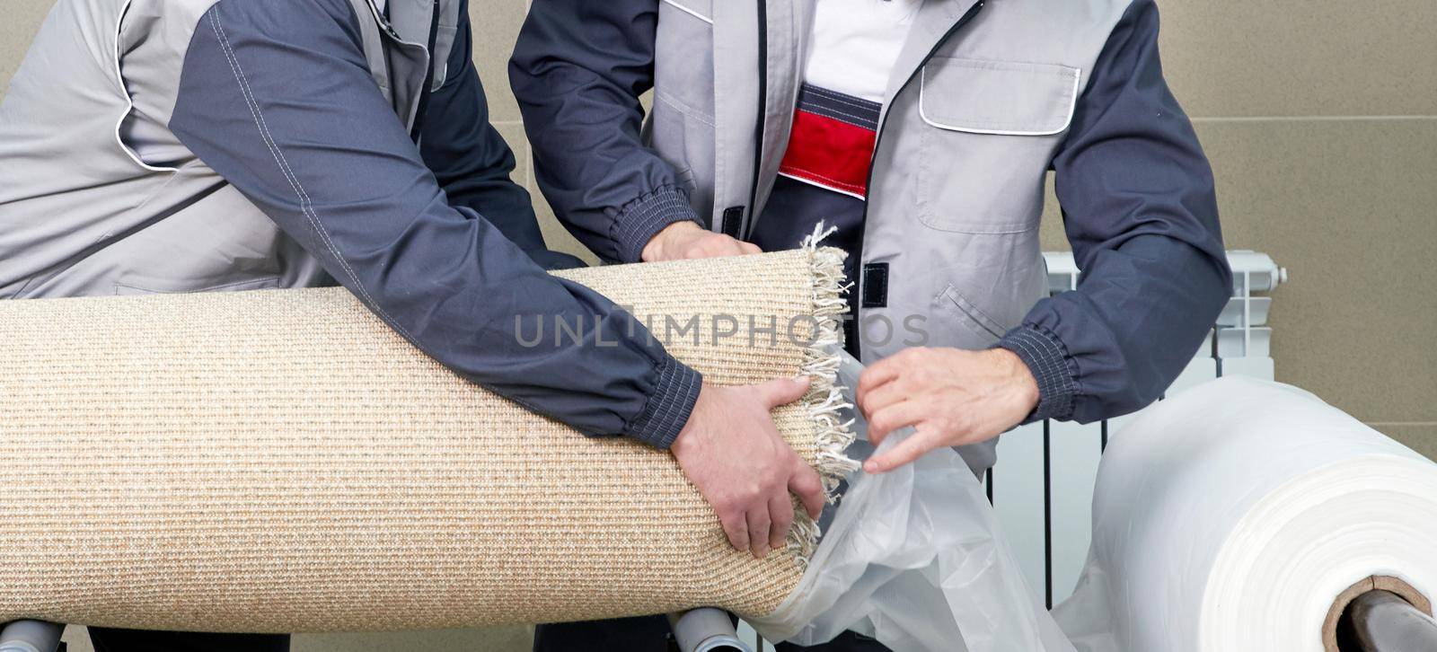 Men workers packing carpet in a plastic bag after cleaning it in automatic washing machine and dryer in the Laundry service by Mariakray