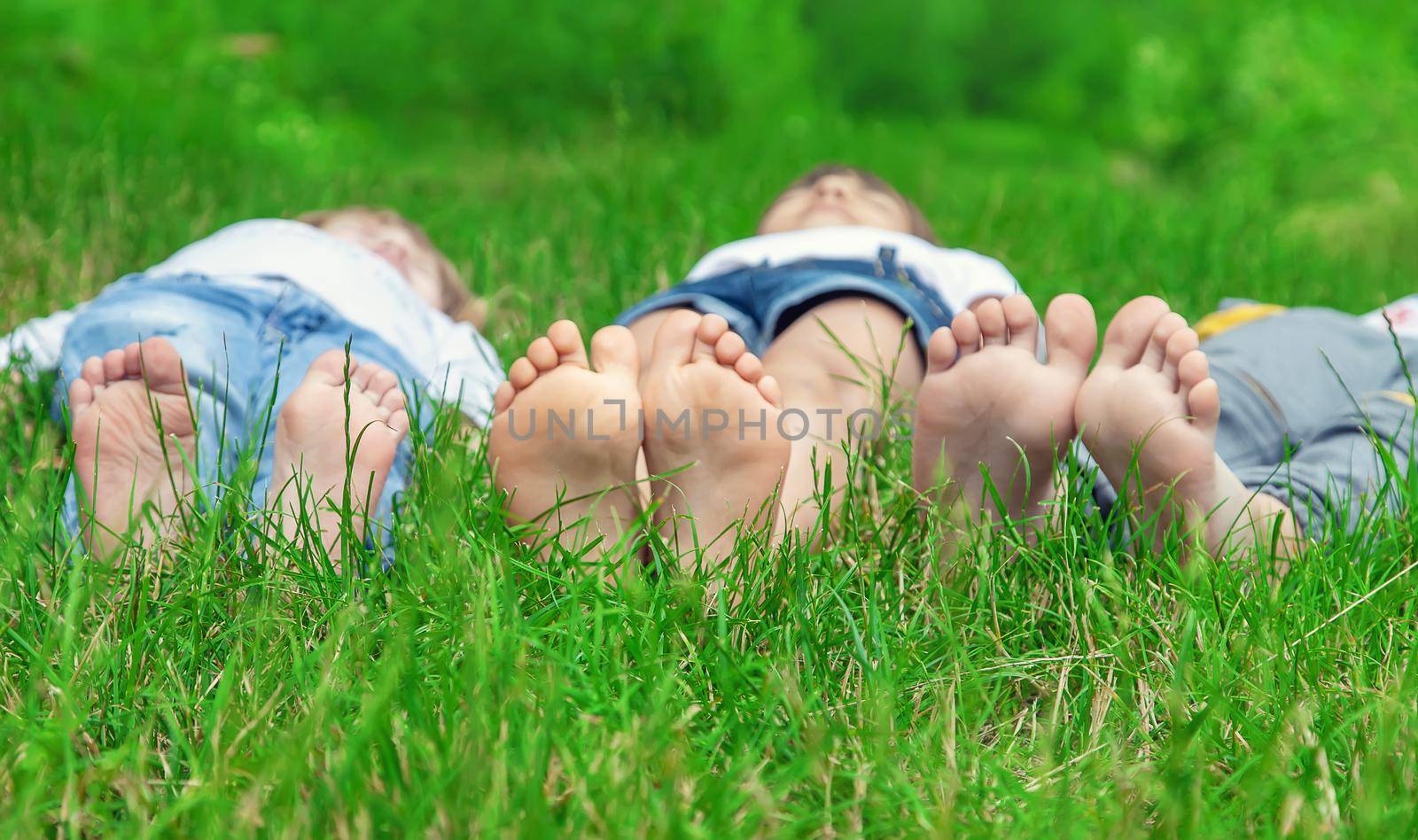 Children's feet on the green grass in the park. Selective focus. by yanadjana