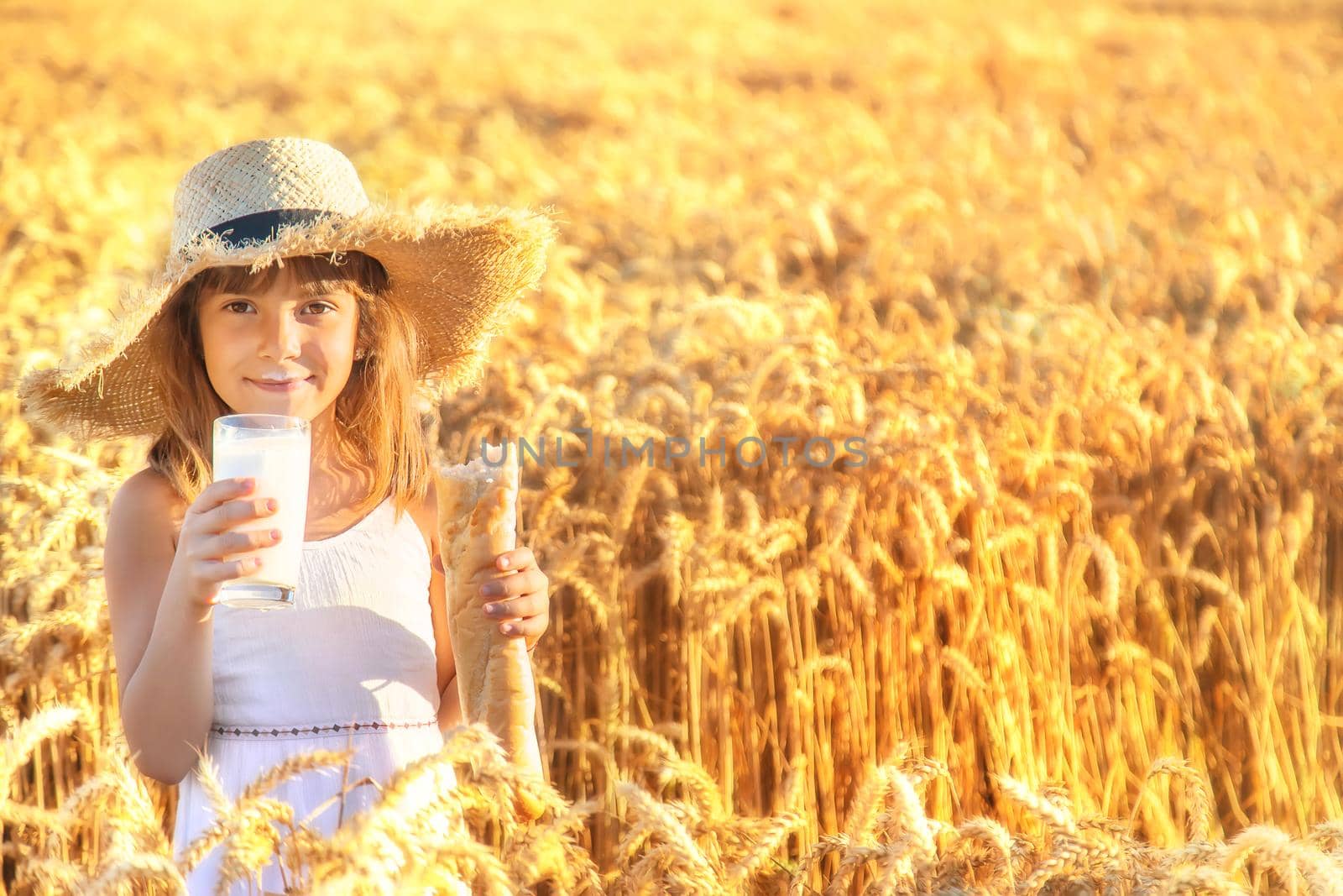 Child with bread and milk in a wheat field. Selective focus. by yanadjana