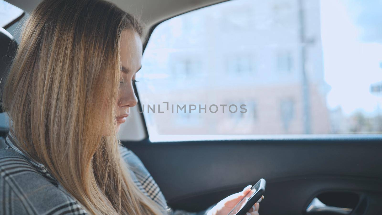 A young girl rides in the backseat of a car and watches her smartphone