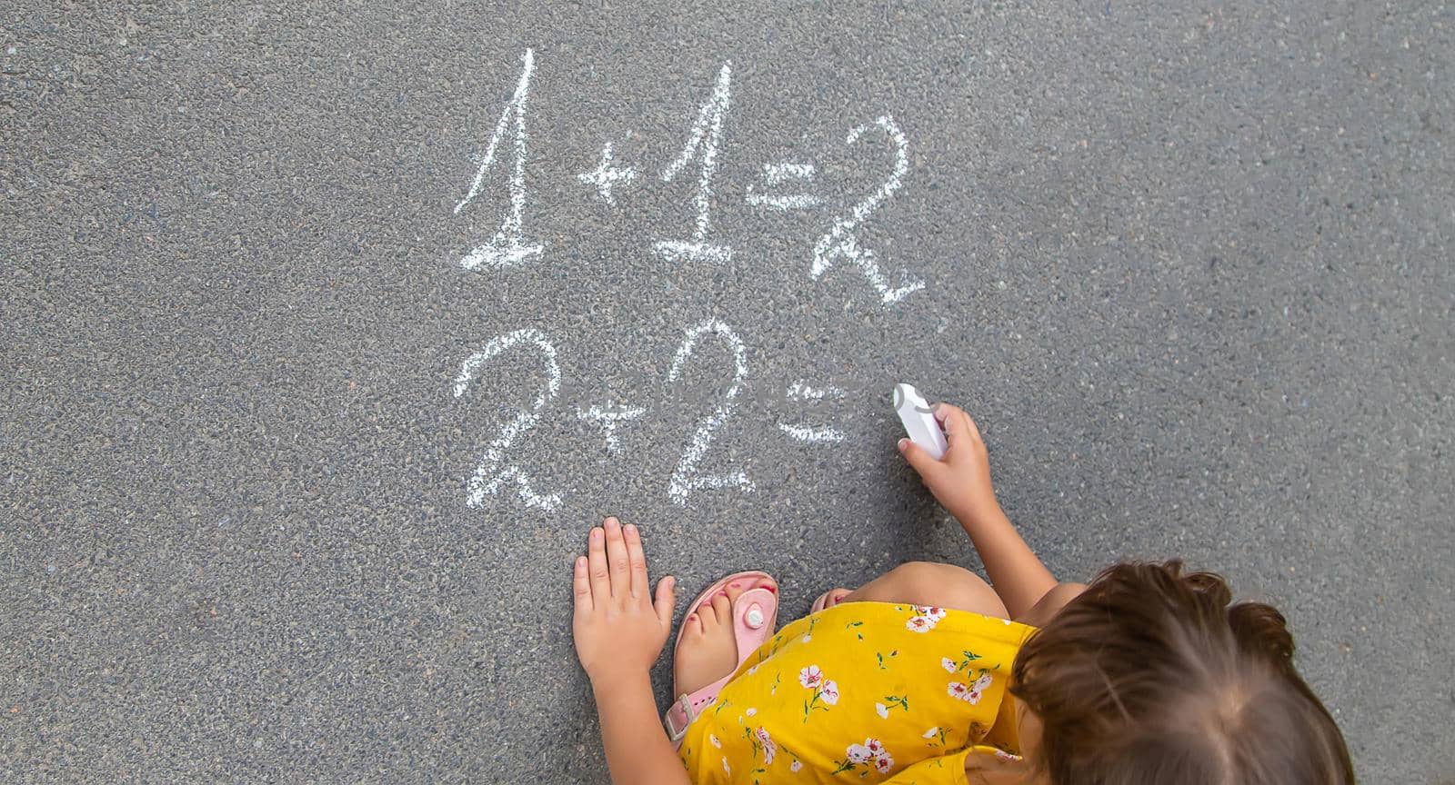 The child writes math on the pavement. Selective focus. by yanadjana