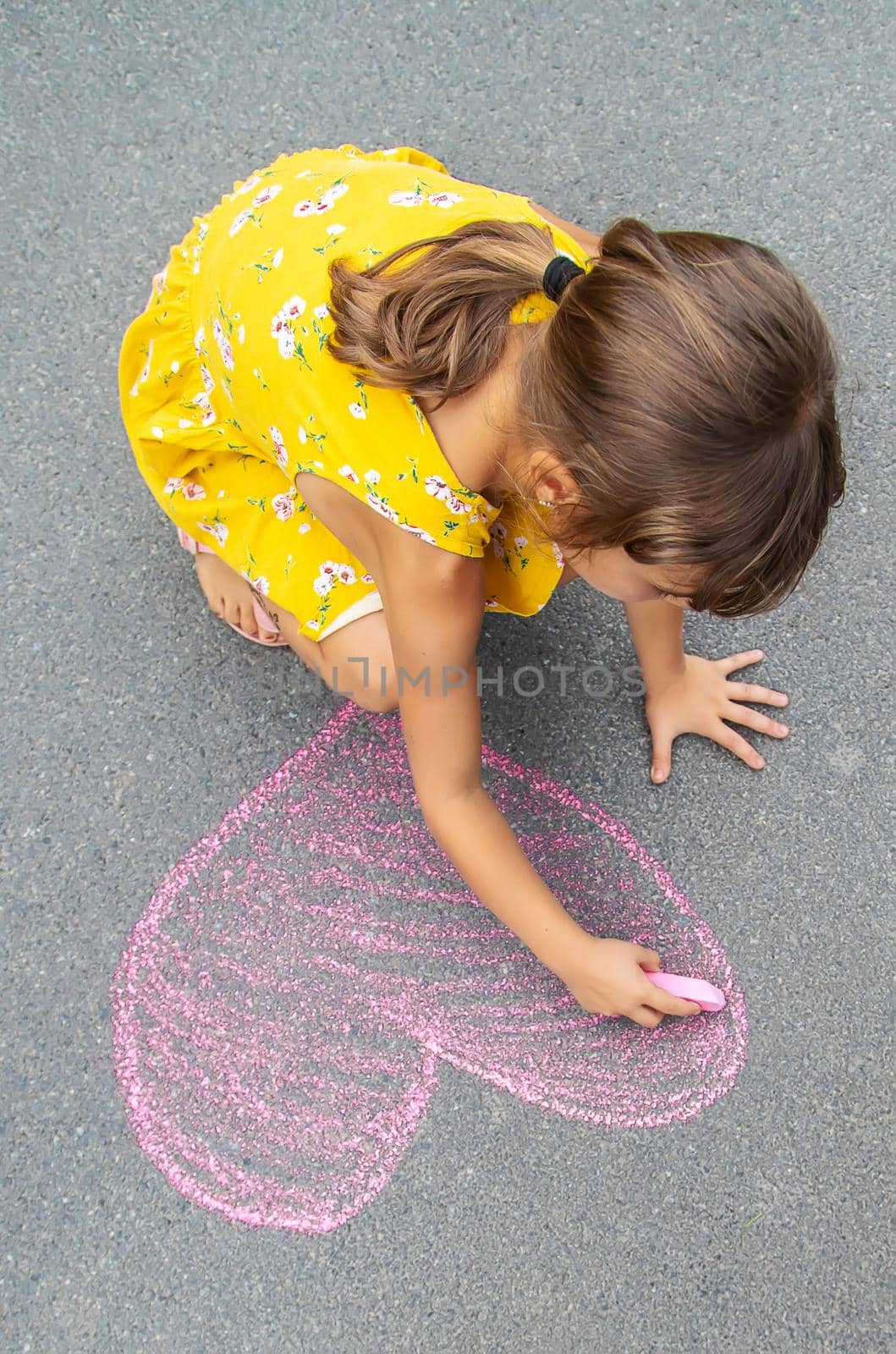 The child draws a heart on the asphalt with chalk. Selective focus. Kid.