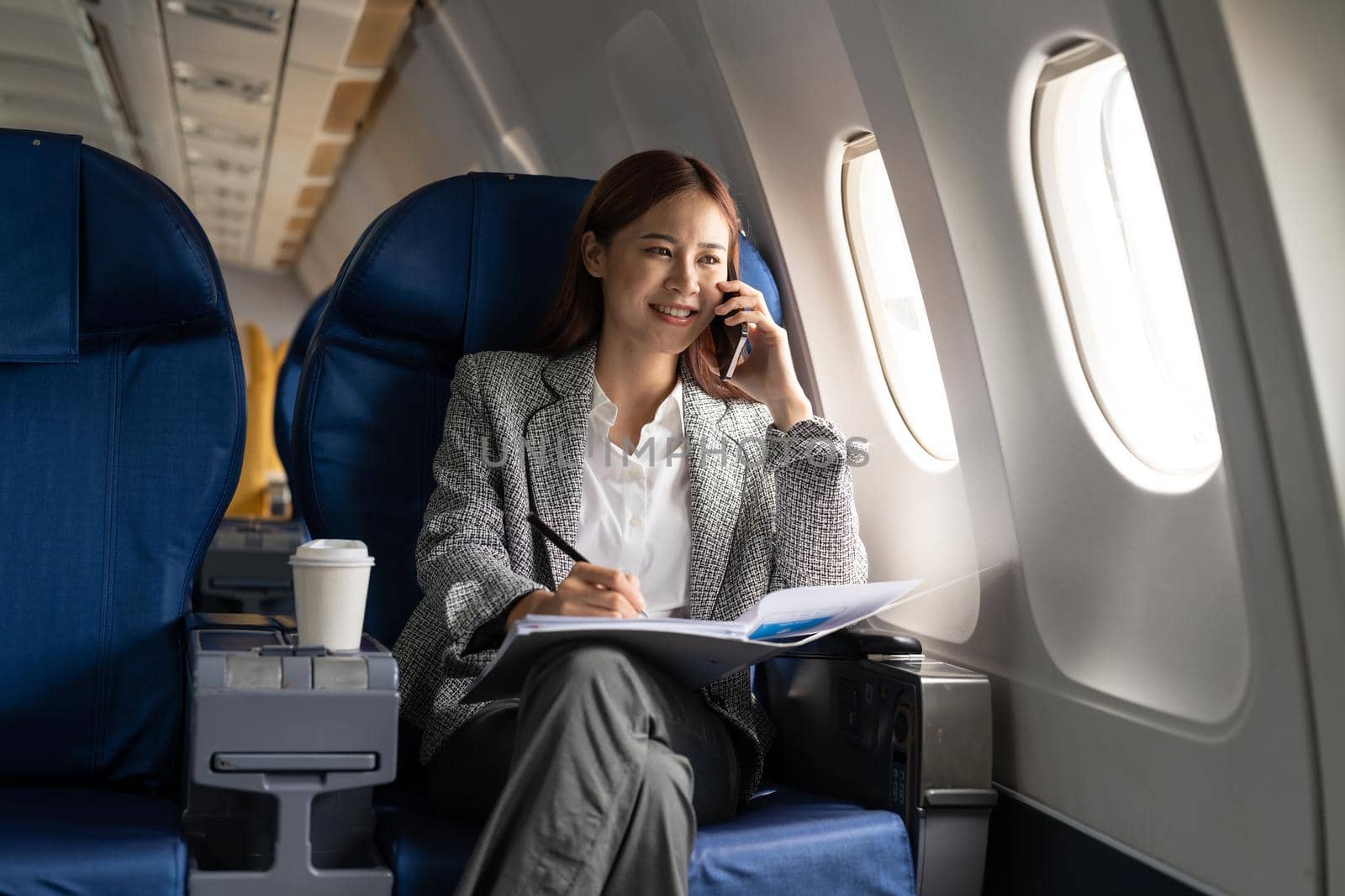 Young attractive and successful business asian woman talking on the phone and working while sitting in the chair of his private business plane.