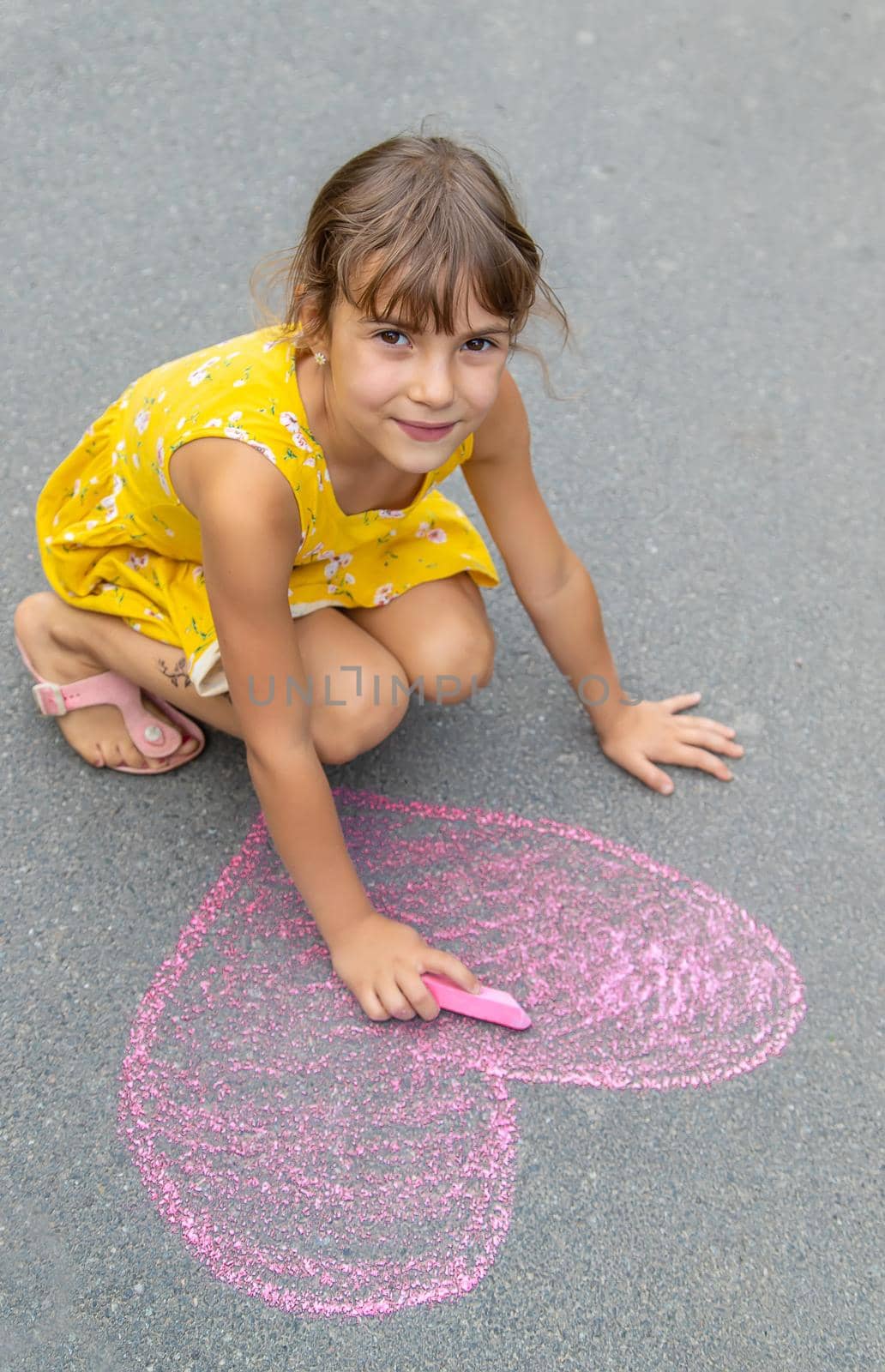 The child draws a heart on the asphalt with chalk. Selective focus. by yanadjana