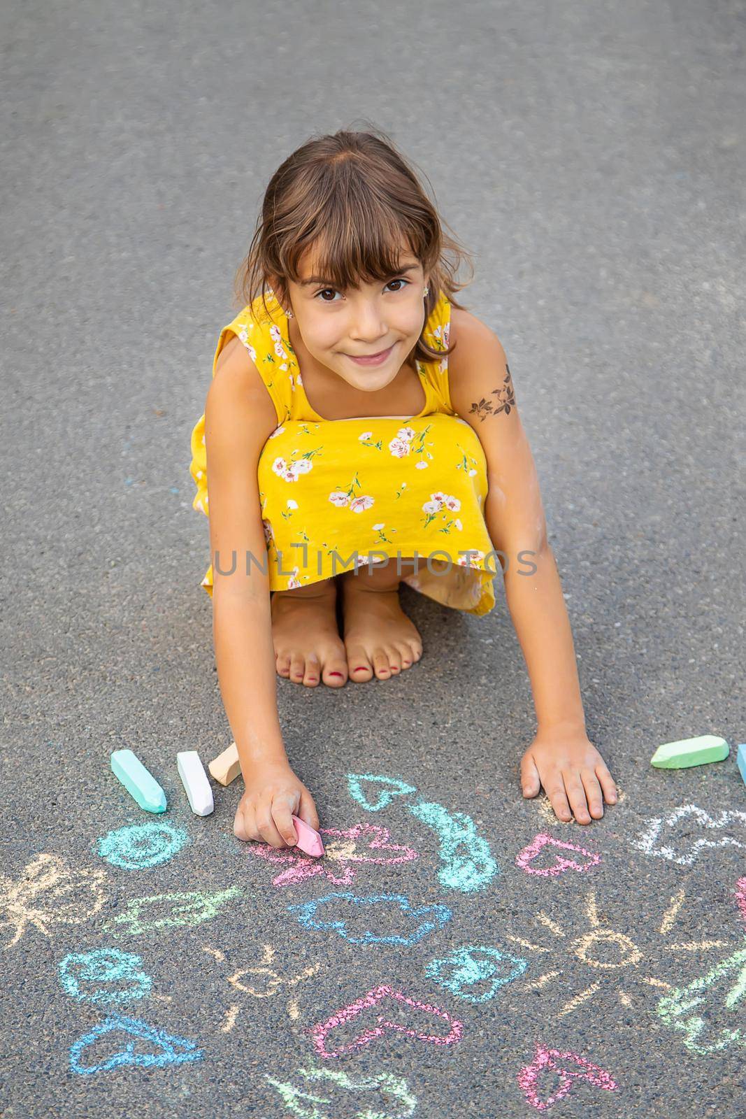 The child draws on the asphalt with chalk. Selective focus. Kid.