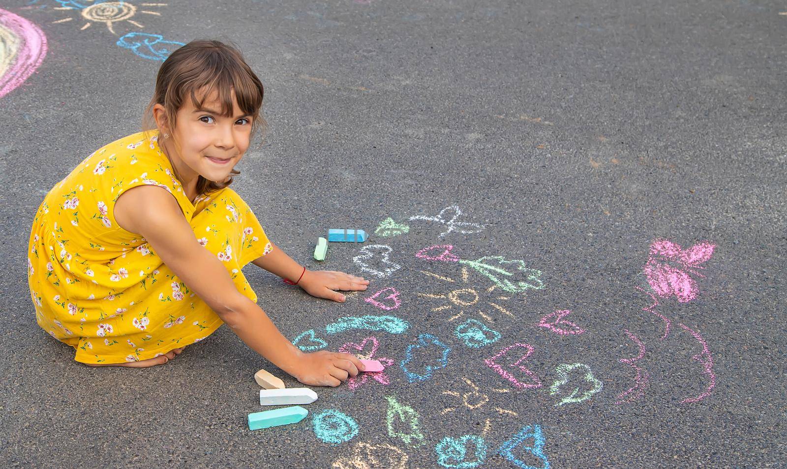 The child draws on the asphalt with chalk. Selective focus. Kid.