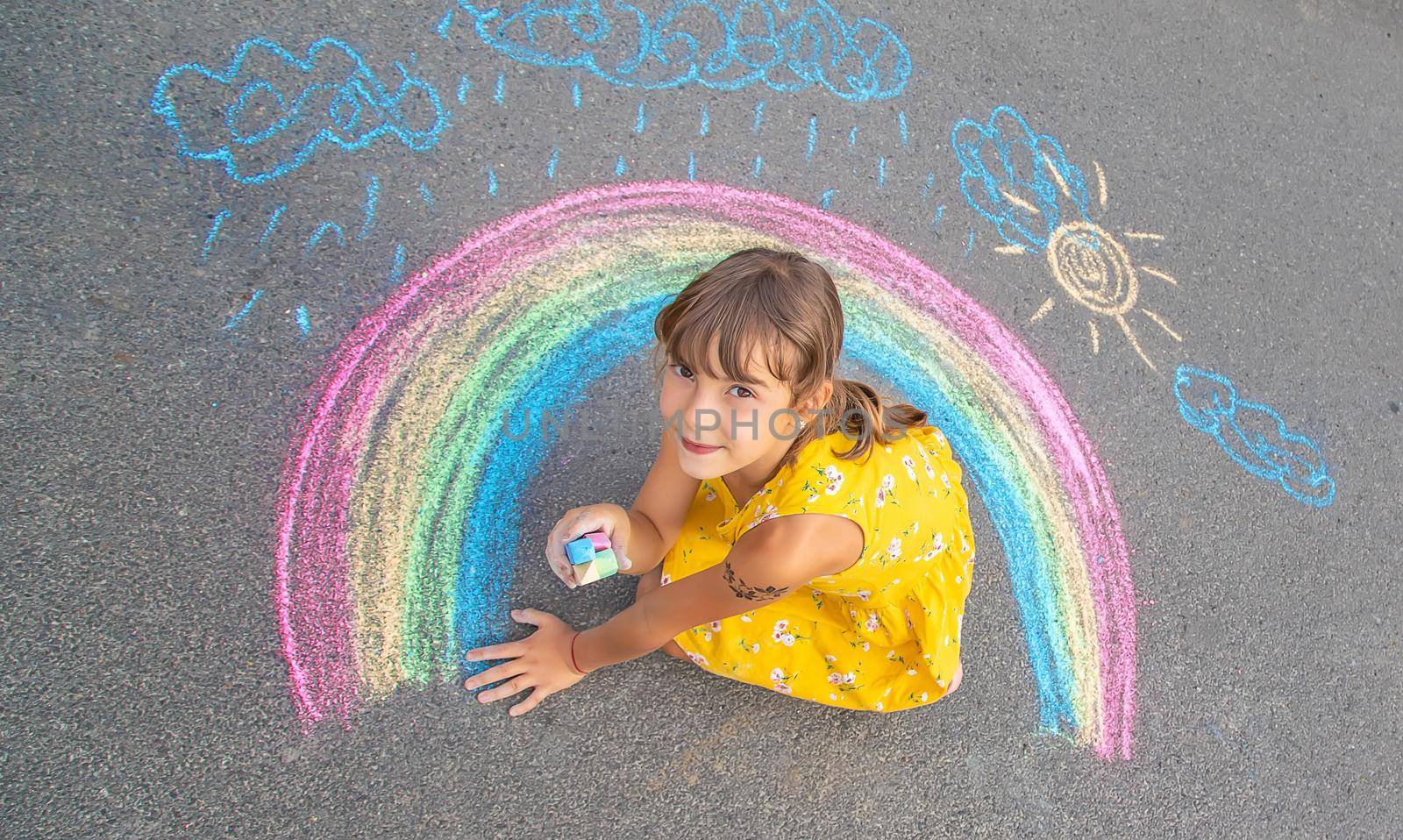 A child draws a rainbow on the asphalt. Selective focus. by yanadjana