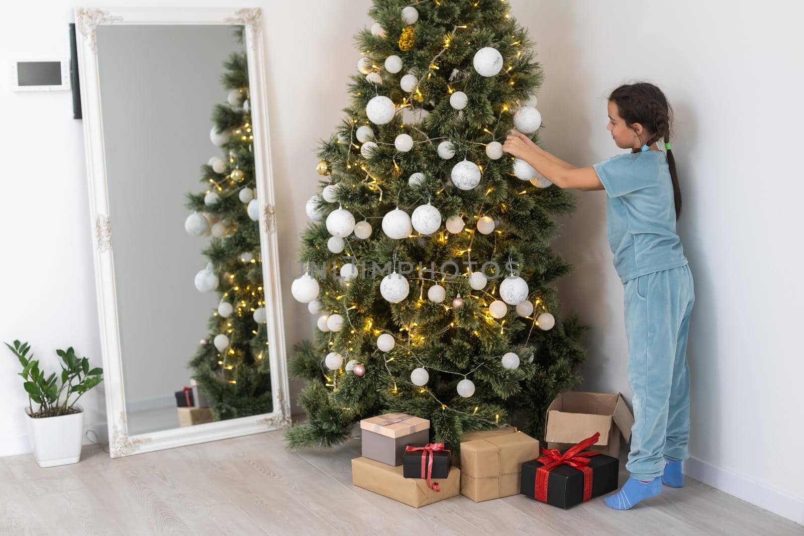 Little girl decorating christmas tree with toys and baubles. Cute kid preparing home for xmas celebration.