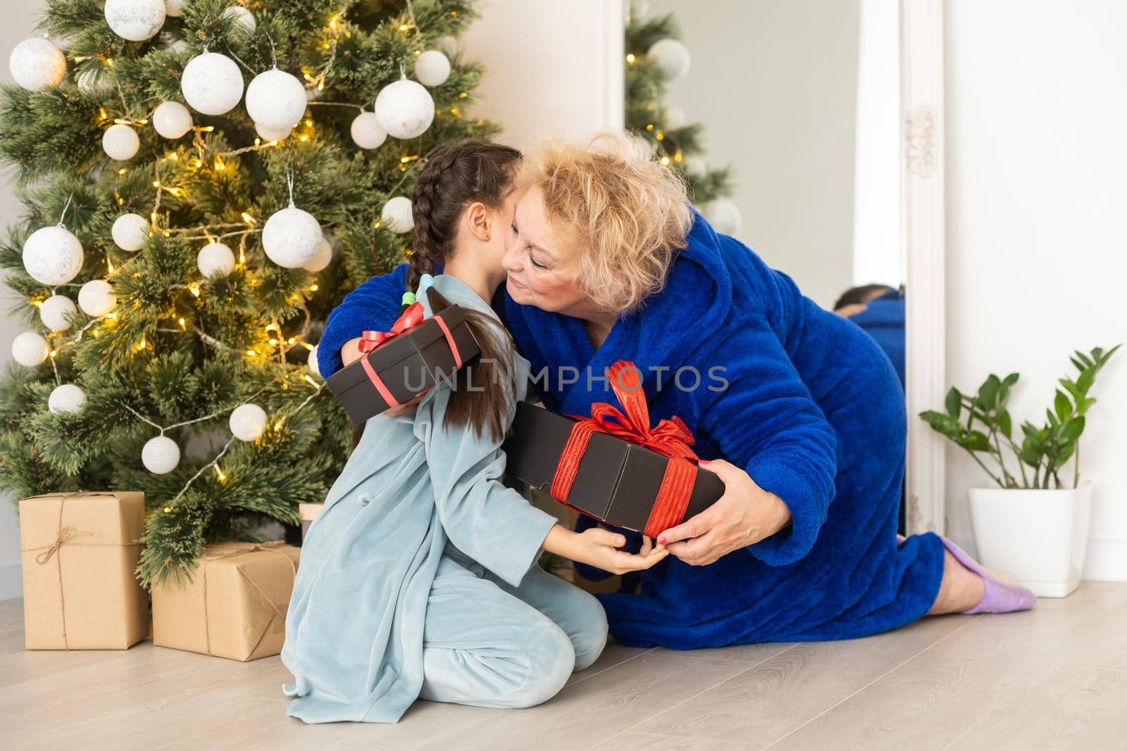 winter holidays and family concept - happy grandmother and baby granddaughter near christmas tree at home.