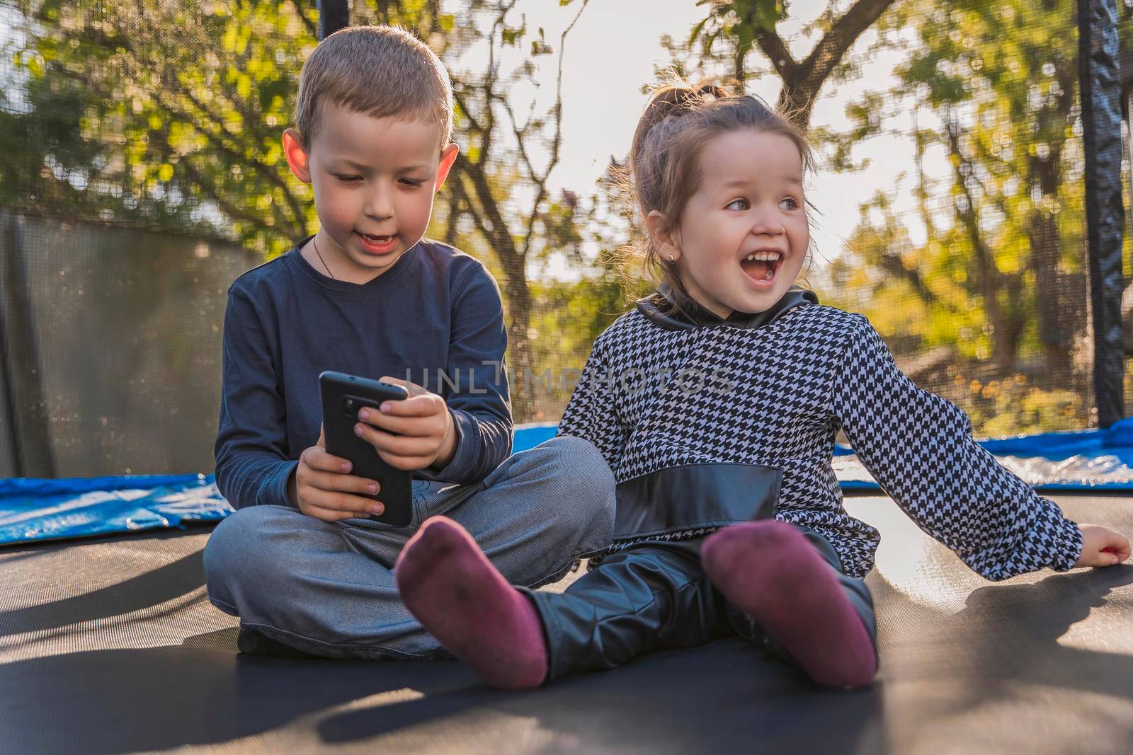 children sit on a trampoline and look at the phone