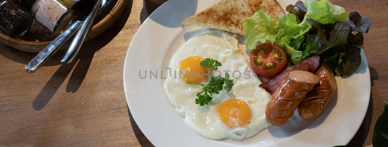 English breakfast with fried eggs, roasted bacon, toasts, sausages and fresh salad on wooden table.