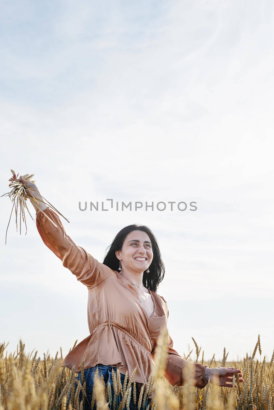 Mid adult woman in beige shirt standing on a wheat field with sunrise on the background, back view by Desperada