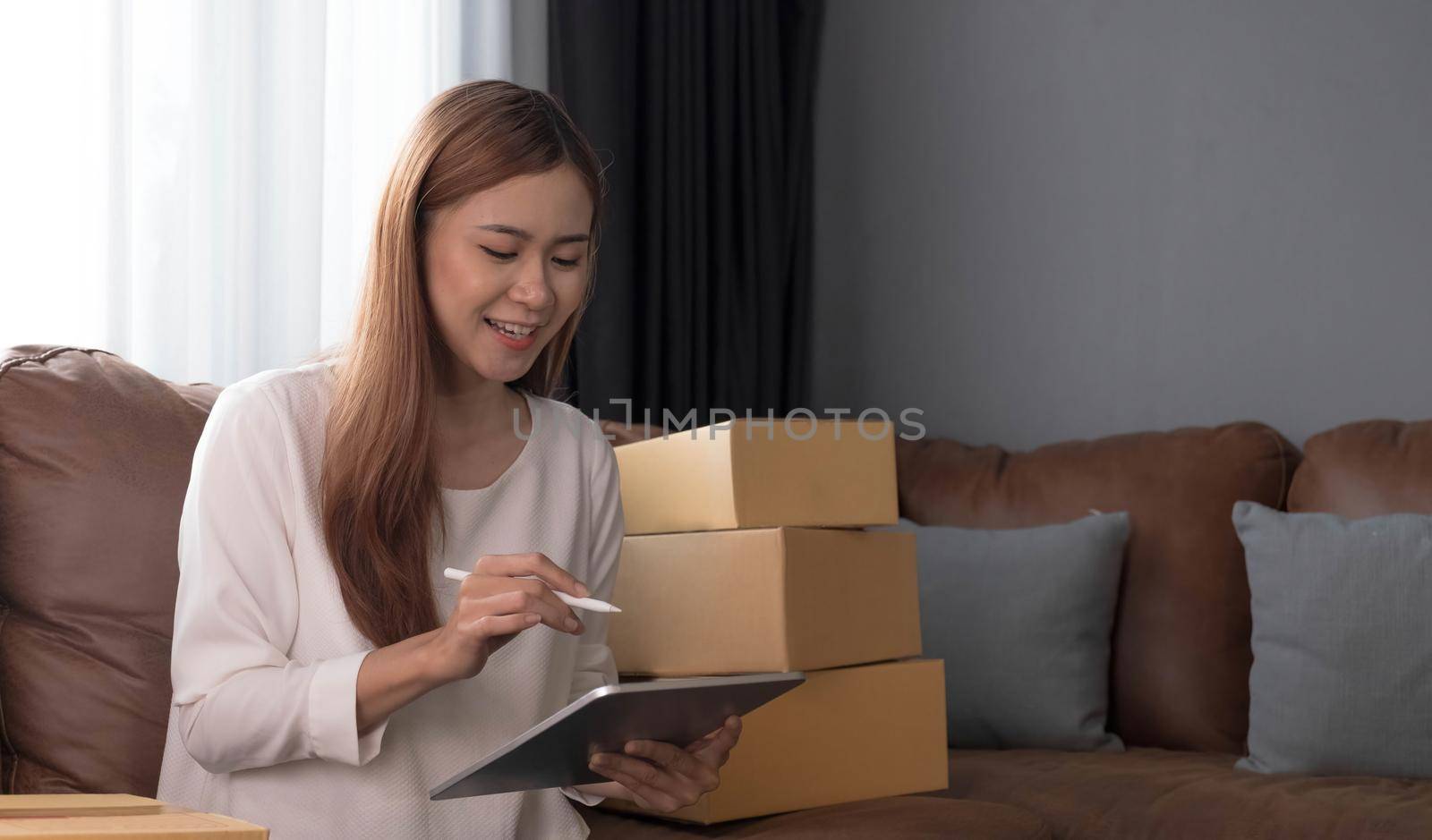 Young asian woman is entrepreneur work from home with online on laptop, online shopping, logistic and delivery, female is seller working on sofa, business SME by wichayada