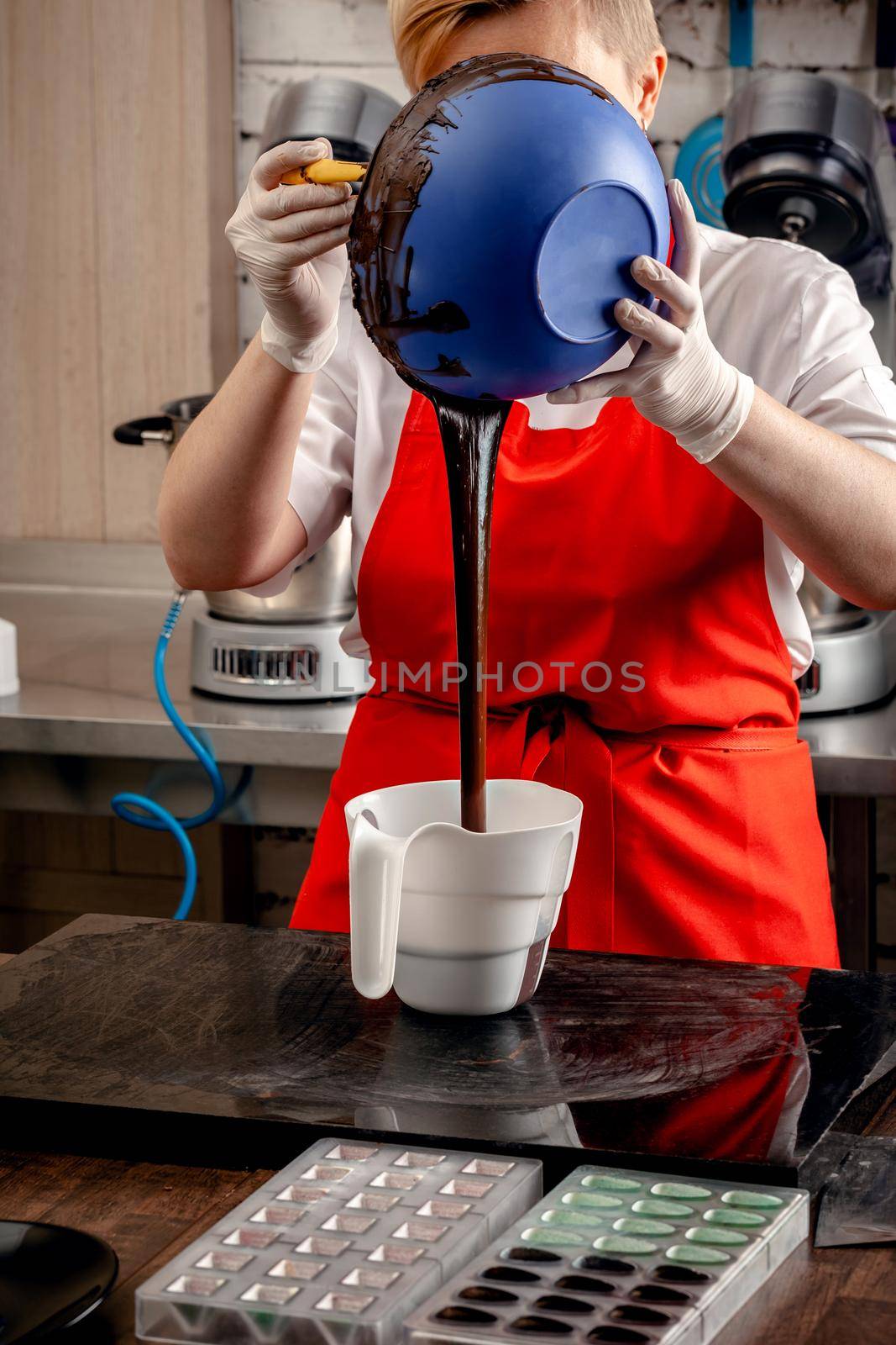 A woman confectioner with red uniform and white sterile gloves preparation of black designer candies. Preparation of chocolate glaze decorations for candy.