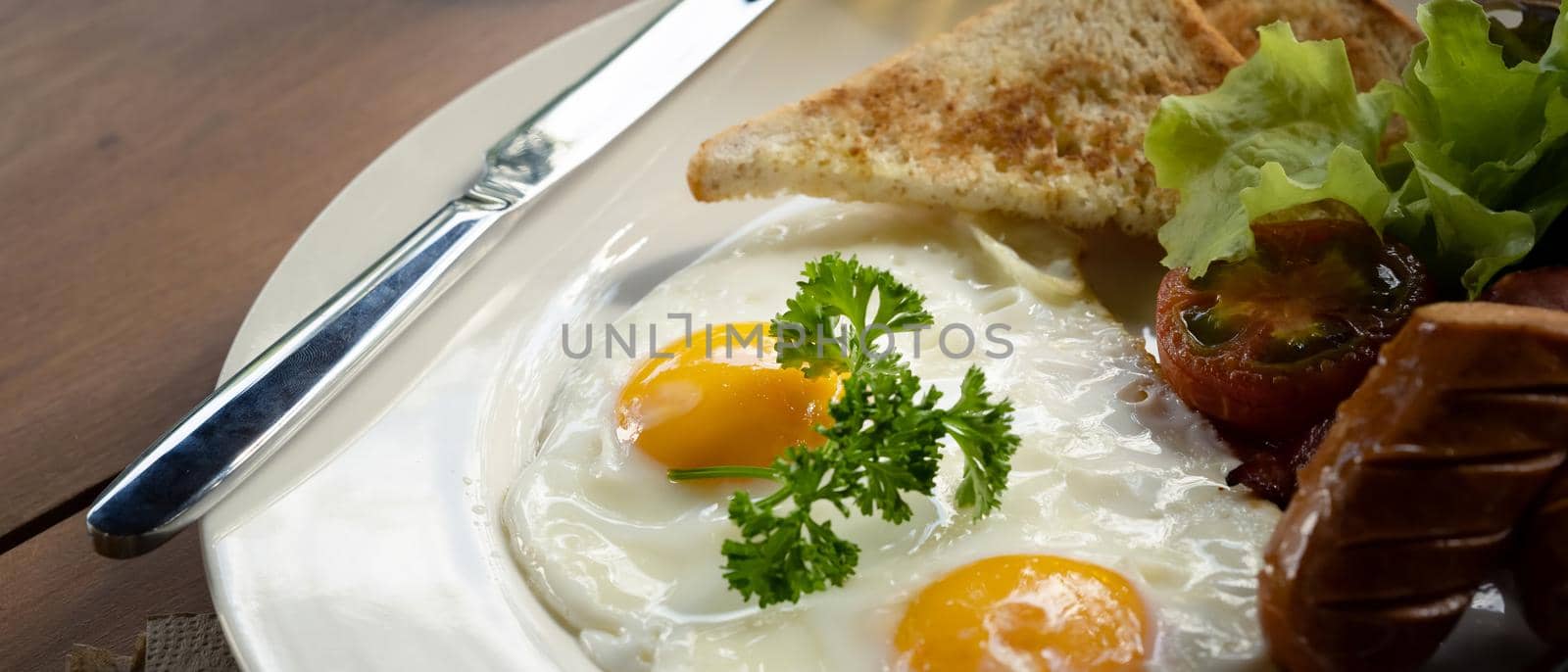 Close up fried eggs, roasted bacon, toasts, sausages and fresh salad for healthy breakfast.