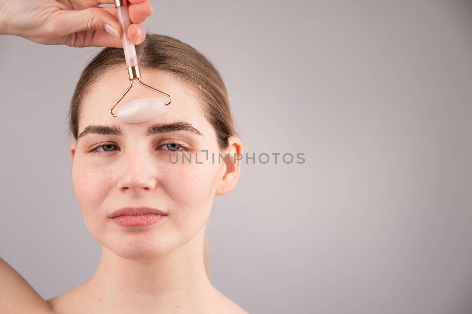 Close-up portrait of a woman uses a quartz roller massager to smooth wrinkles on her forehead. by mrwed54