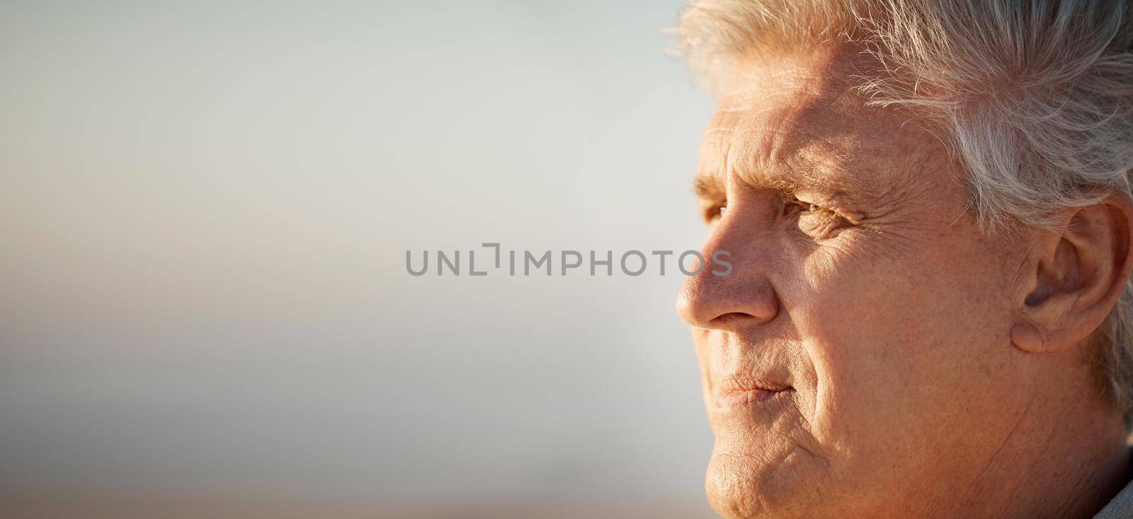 Mature man enjoying the view on the beach. Senior man looking at the view on the beach. Mature man on holiday by the beach. Closeup on face of older man enjoying a holiday on the beach