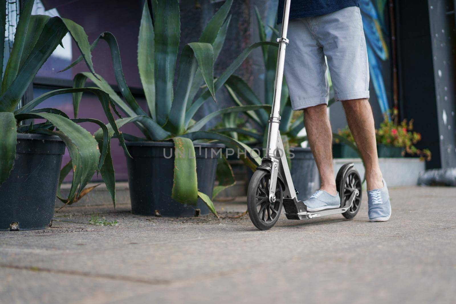 Close up of man feet stand on town adult scooter with big wheels in a stylish sneakers having a ride on the streets or park after work outdoors. No face visible by LipikStockMedia