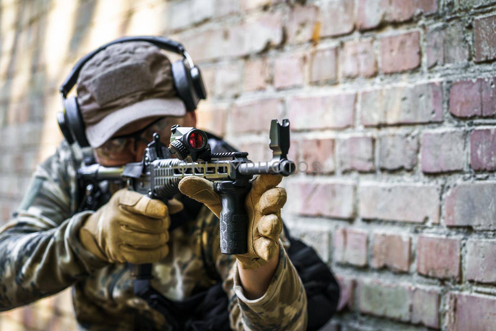 Training cycle in-service for civil police troops. Young man with gun standing sideways near brick wall during advanced firearms, defense tactics, use of force policy review, officer safety updates by LipikStockMedia