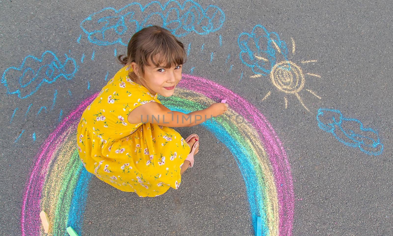 A child draws a rainbow on the asphalt. Selective focus. by yanadjana