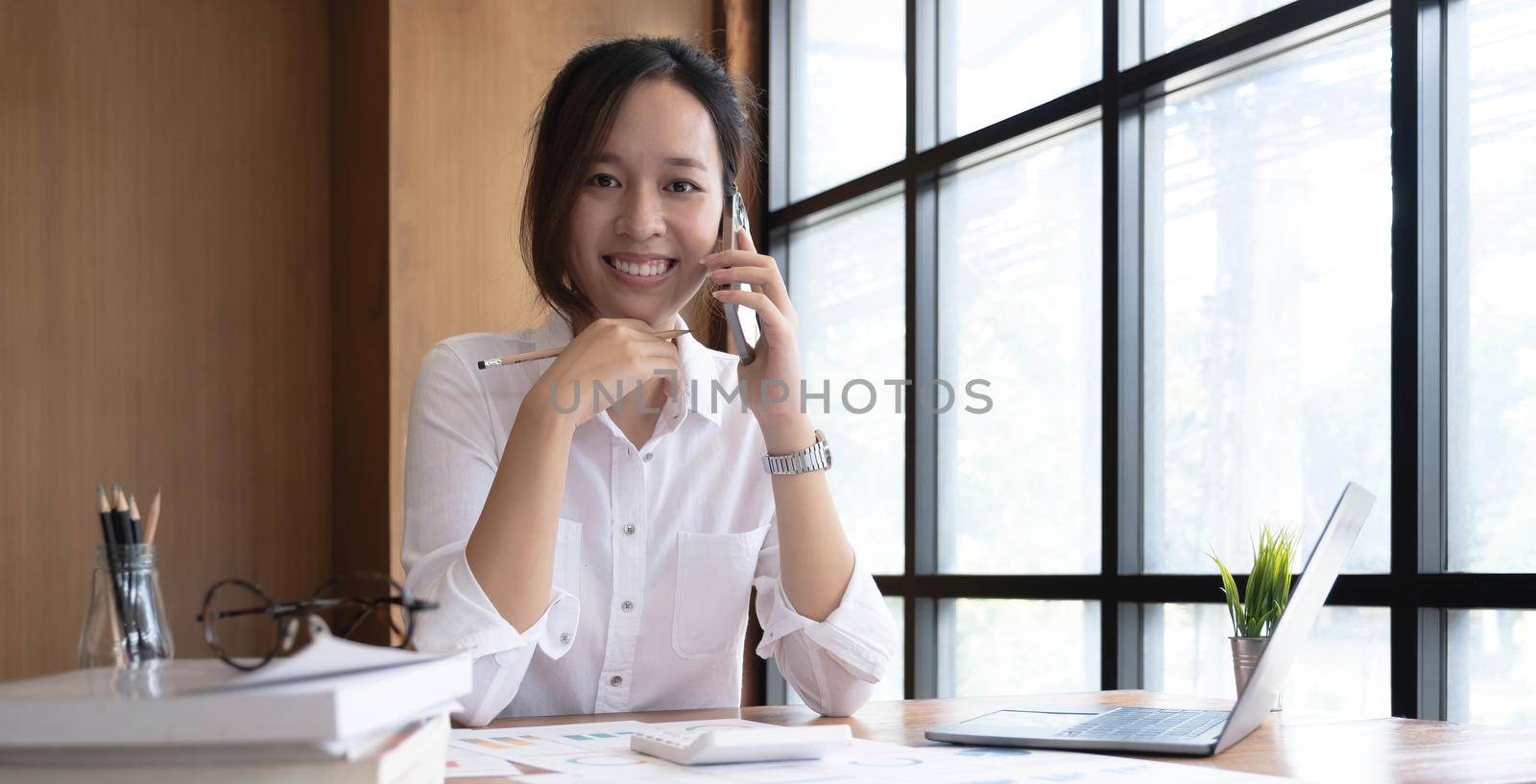 Asian business woman have the joy of talking on the phone, laptop and tablet on the office desk. by wichayada