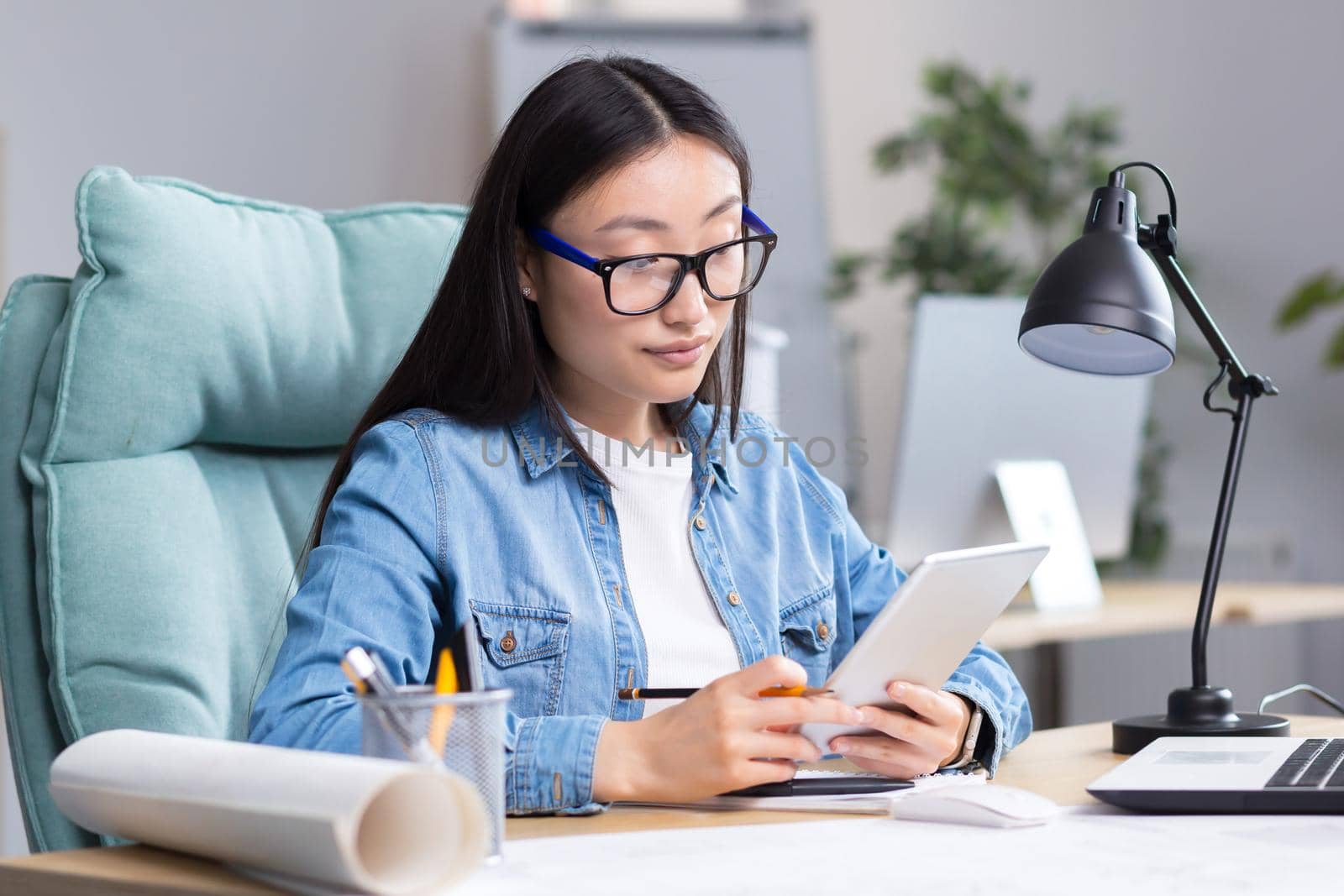 Young Asian woman designer working in office using tablet, working on drawing project.