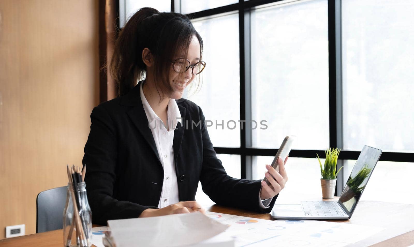 Young asian businesswoman beautiful charming smiling and using on mobile phone in the office. by wichayada
