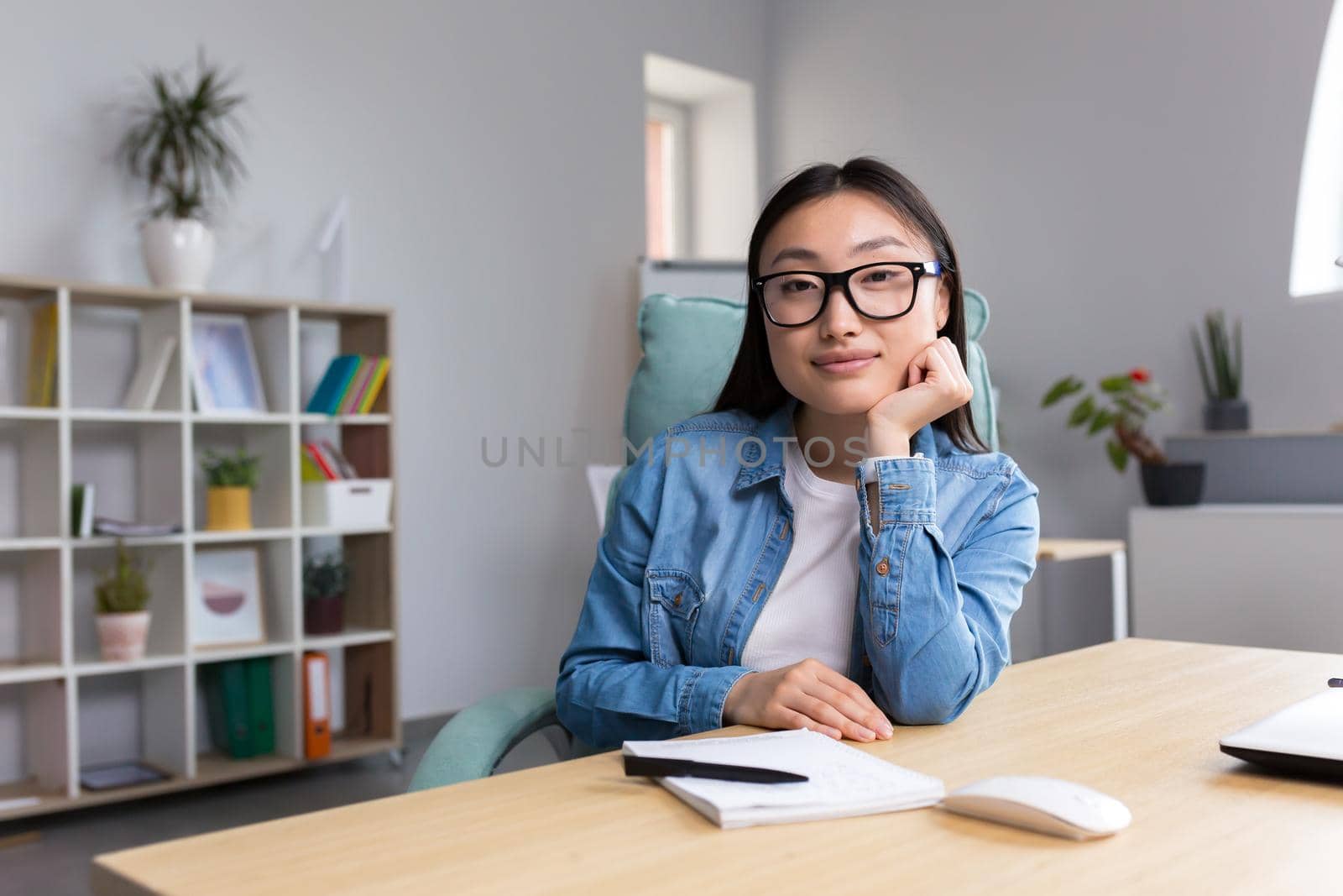 Portrait of young business woman in modern office, Asian looking at camera smiling.