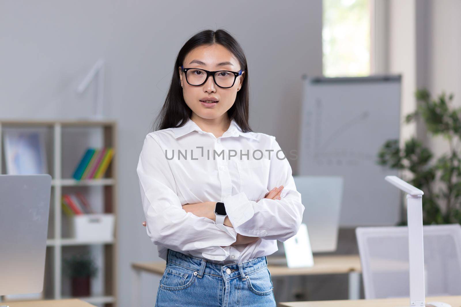 Portrait of a young Asian business woman, a worker in the office with crossed arms looking at the camera.