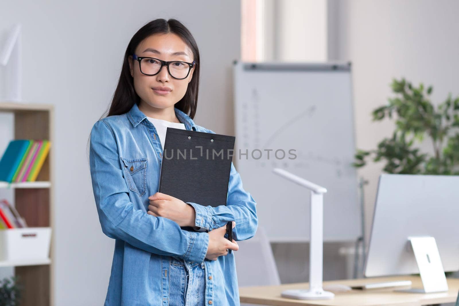 Young beautiful Asian female teacher looking at the camera and smiling, portrait of a woman in the office.