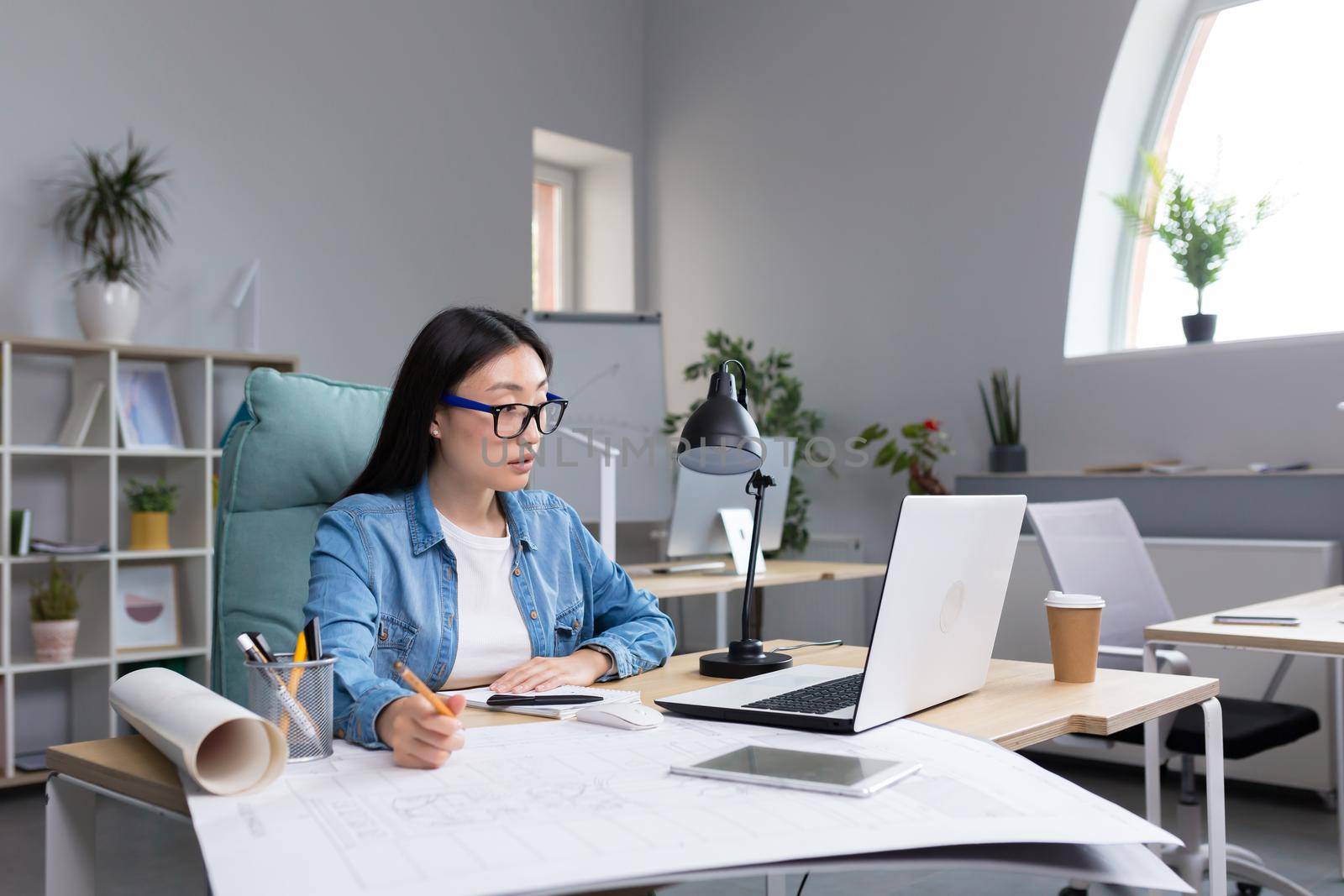 Young beautiful Asian female architect working on a project in an architectural office studio.