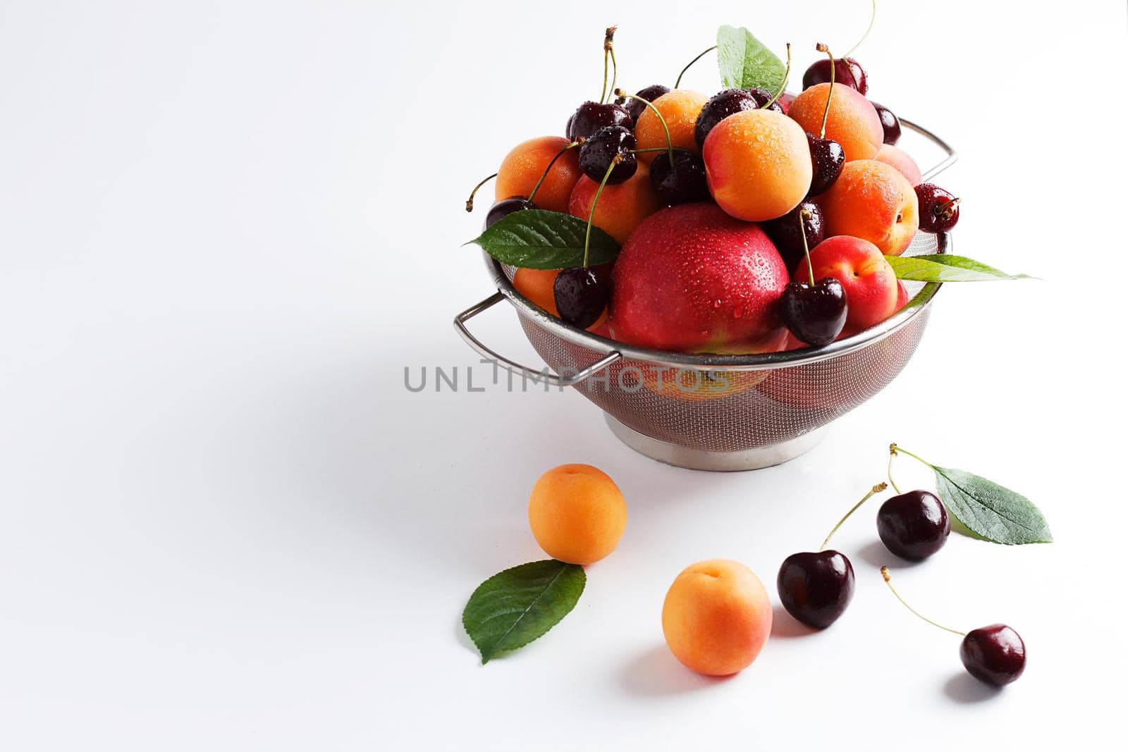 apricots and cherries in a metal bowl on a white background. Copy spase