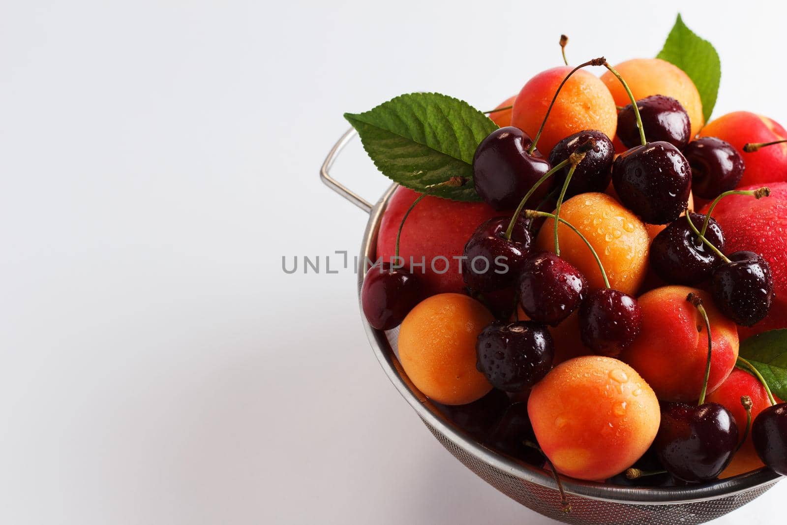 apricots and cherries in a metal bowl on a white background. Copy spase