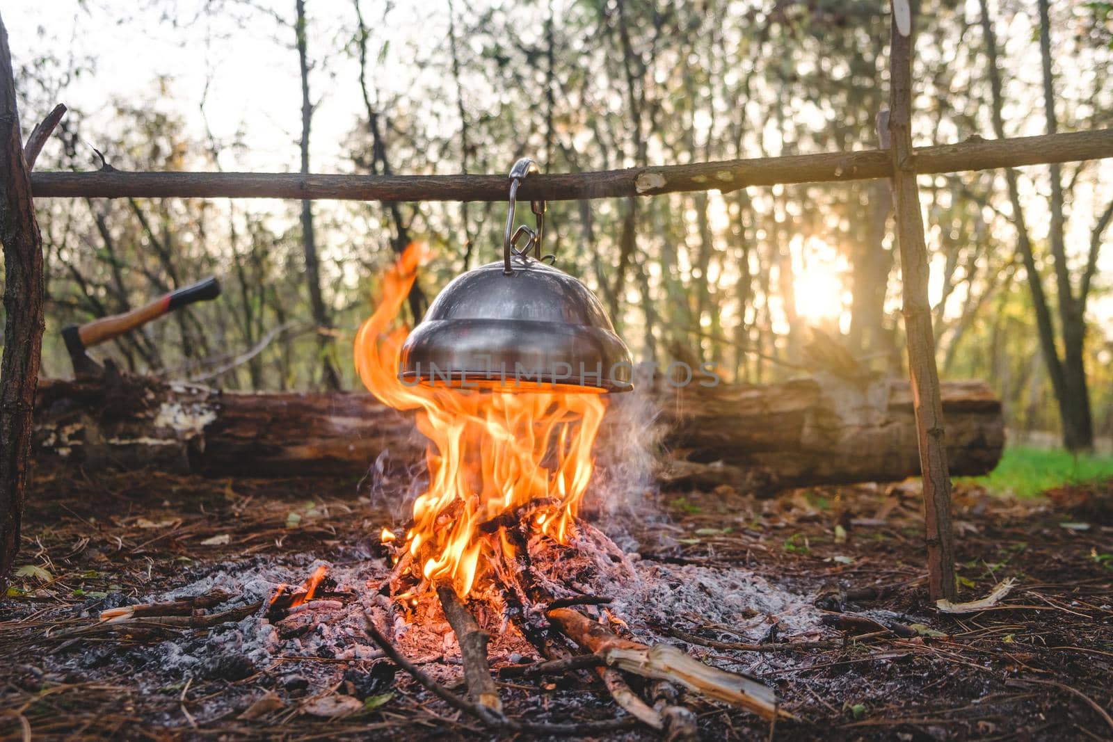 kettle is heated on a bonfire.  travel in the forest. Outdoor recreation concept. Teapot over the fire. Beautiful campfire in a tourist camp in the autumn forest with a hatchet on background by igor010