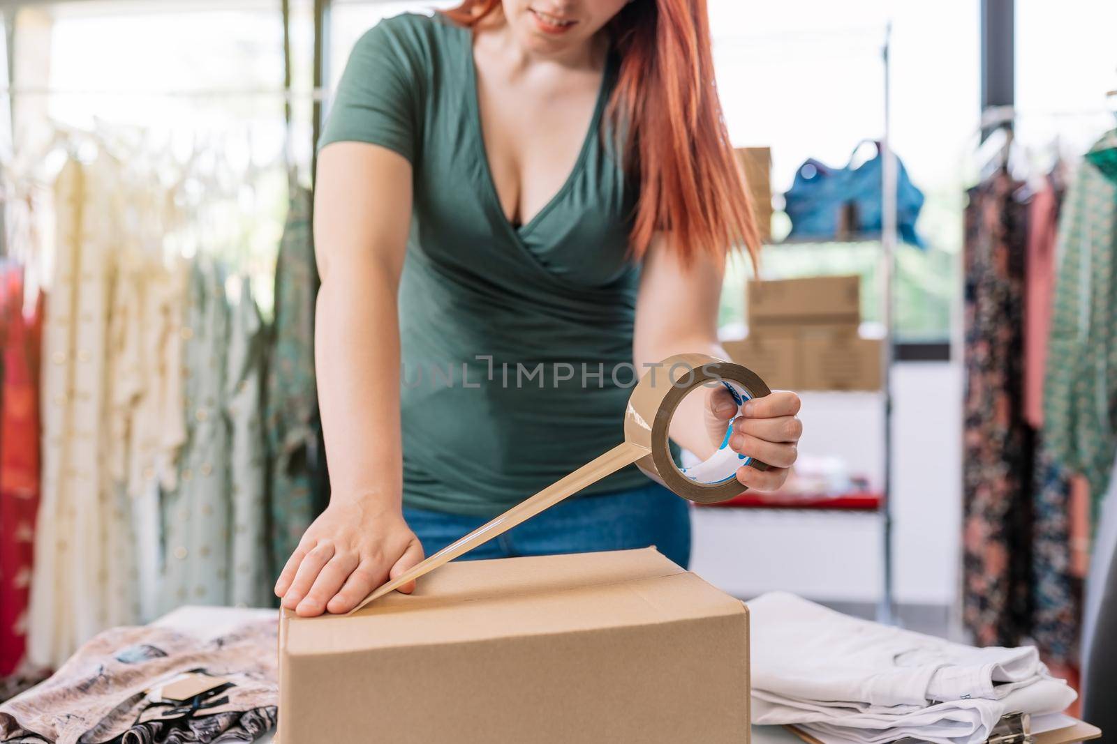 Cutaway view of a young businesswoman, packing a box with tape, for a shipment from her online clothing shop. Young woman preparing a package for a client in the office. work and business concept. by CatPhotography