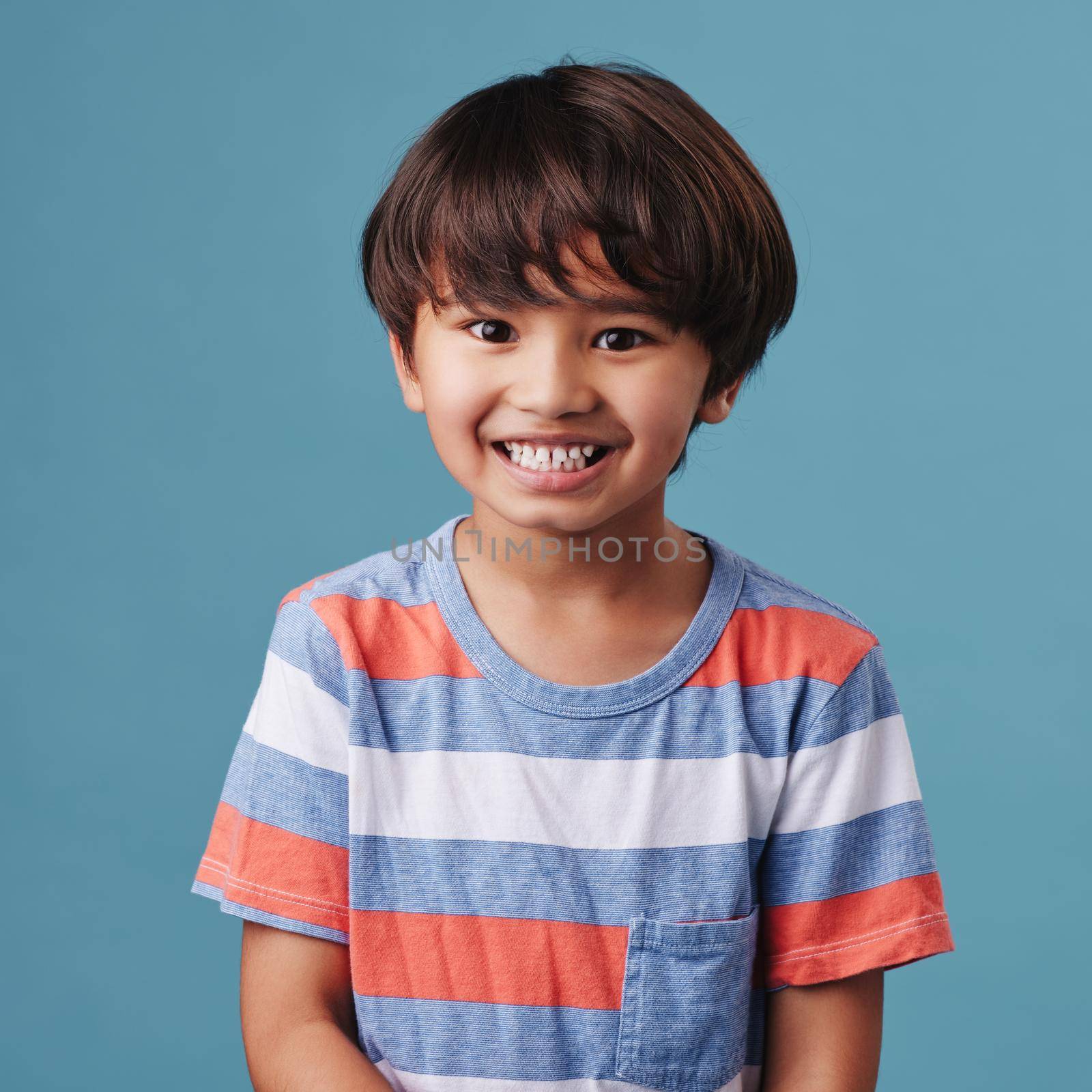 Portrait of a cute little asian boy wearing casual clothes while smiling and looking excited. Child standing against a blue studio background. Adorable happy little boy safe and alone.