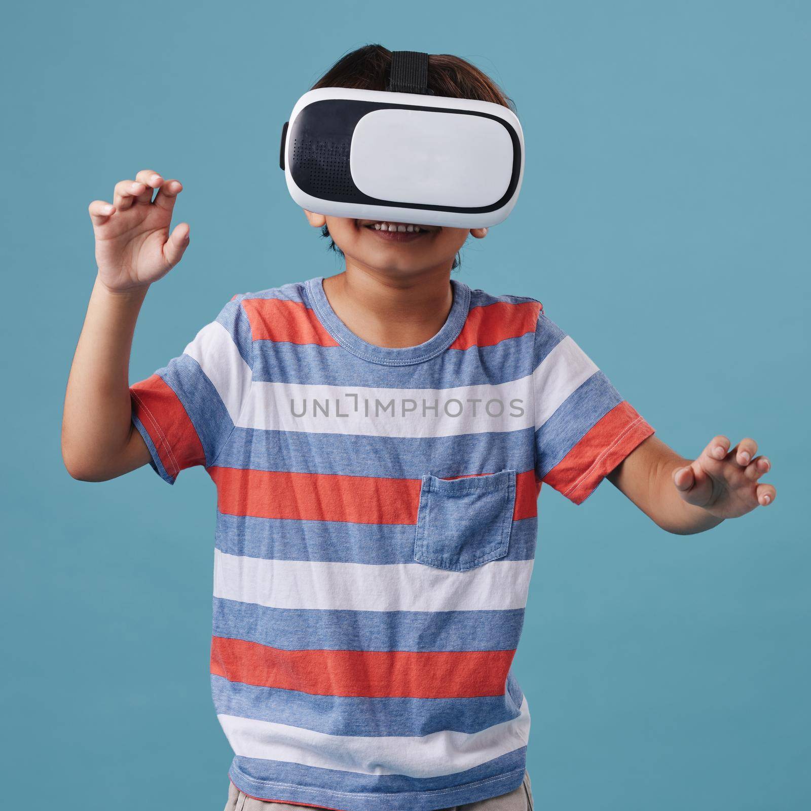 Young mixed race boy standing and wearing a wireless vr headset and playing a video game against a blue background. Fun and games on are for the weekend.