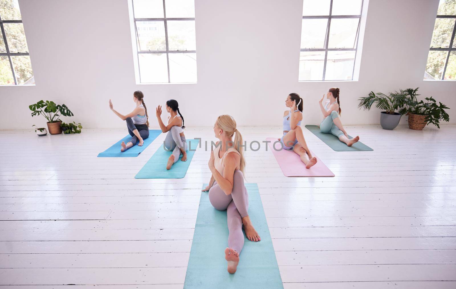 Group of women twisting in yoga studio. Flexible women sitting in yoga pose together. Group of flexible women stretching in pilates studio. Sporty women training together in yoga class.
