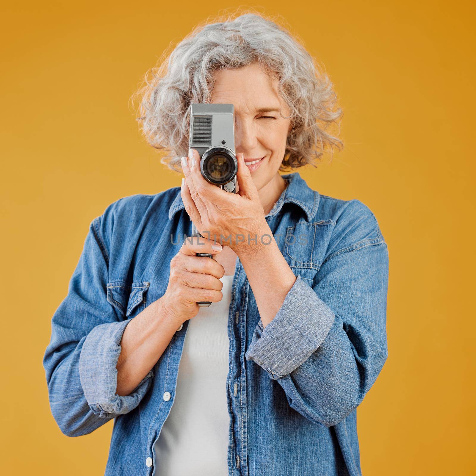 One happy caucasian woman standing against a yellow background in a studio and taking a picture on a camera. Confident cheerful caucasian lady holding a camera and taking a photograph. Smile and pose.