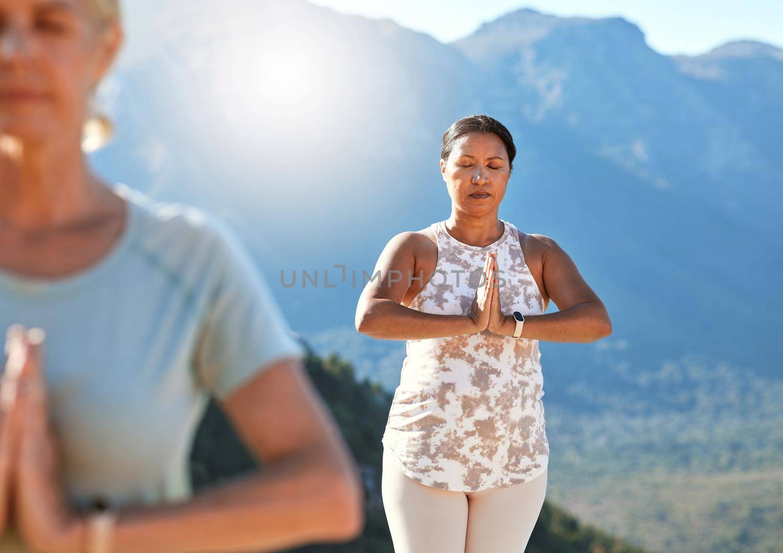 Mature woman meditating with joined hands and closed eyes breathing deeply. Mature people doing yoga together in nature on a sunny day.
