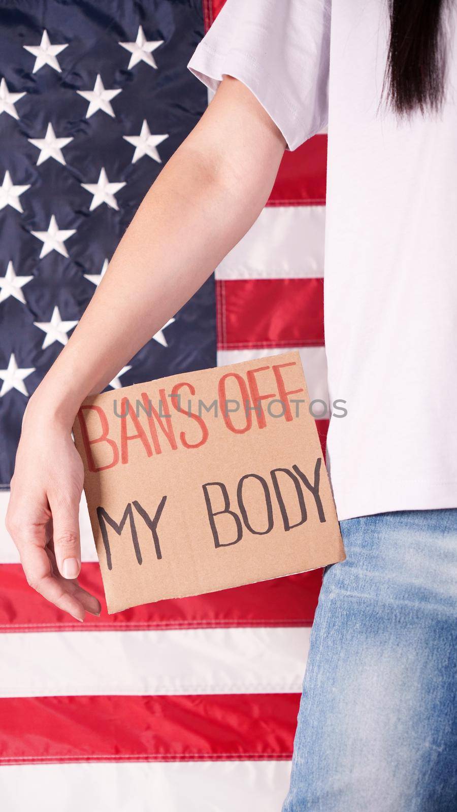 Woman holding a sign Bans Off My Body American flag on background. Protest against anti abortion law. Women's strike. Womens rights freedom