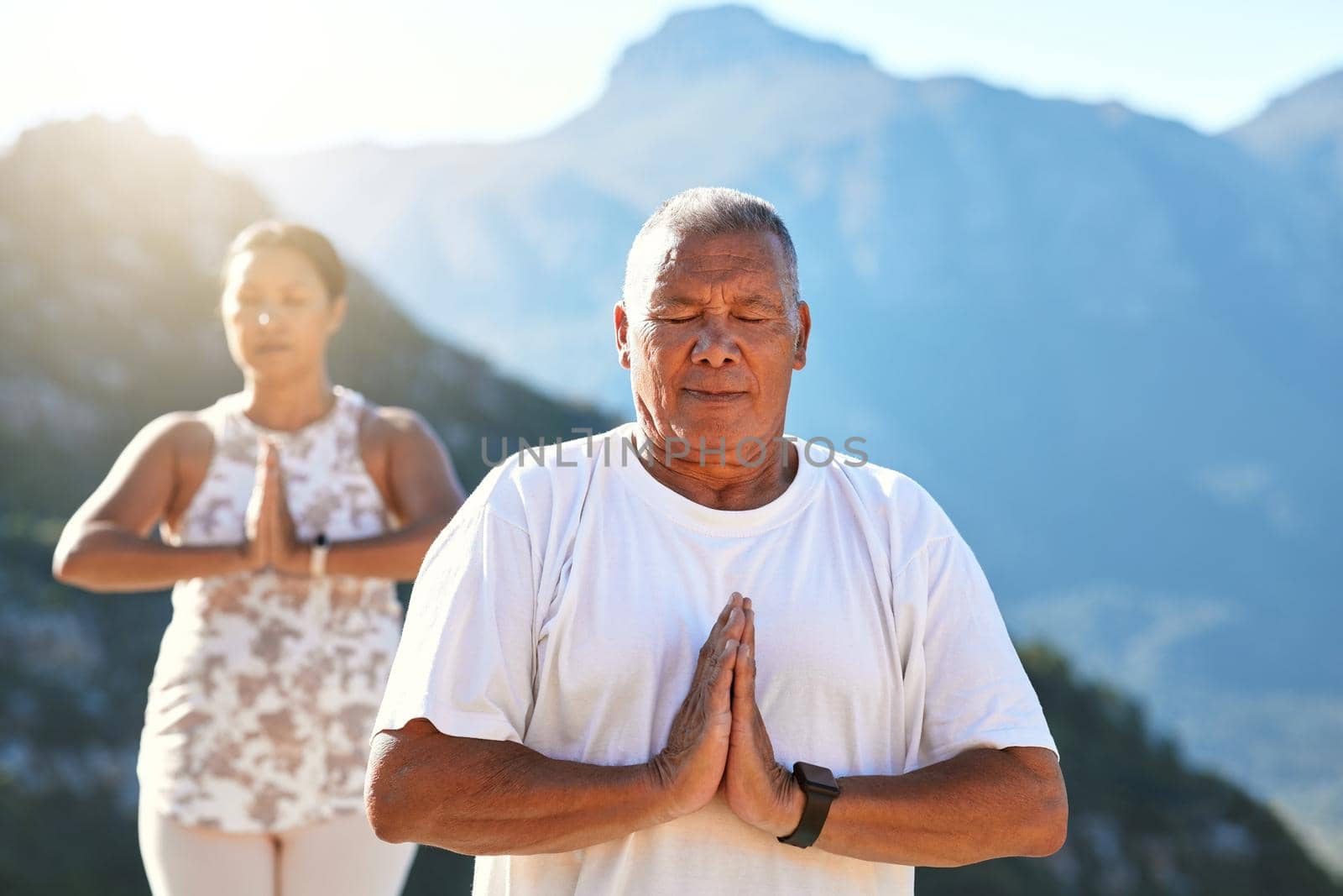 Senior couple meditating with joined hands and closed eyes breathing deeply. Mature couple doing yoga in nature living a healthy active lifestyle in retirement.