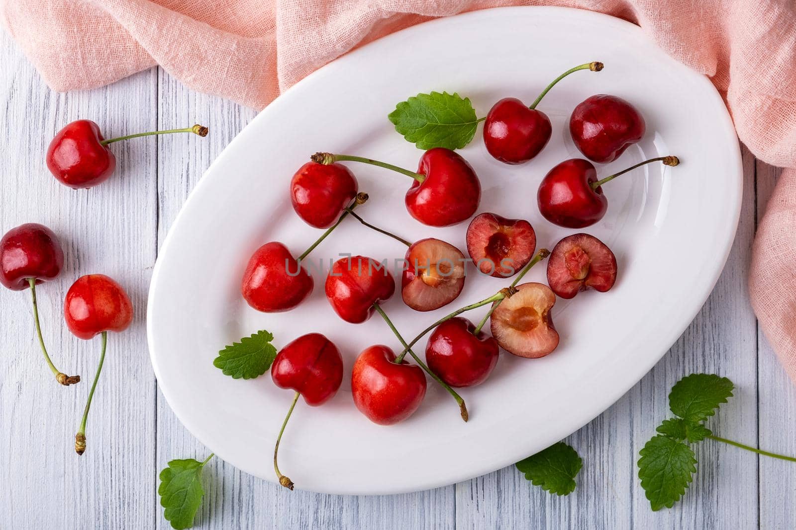 Ripe juicy sweet cherry lies on a white porcelain plate on a light wooden surface. Summer healthy food. Selective focus. View from above.