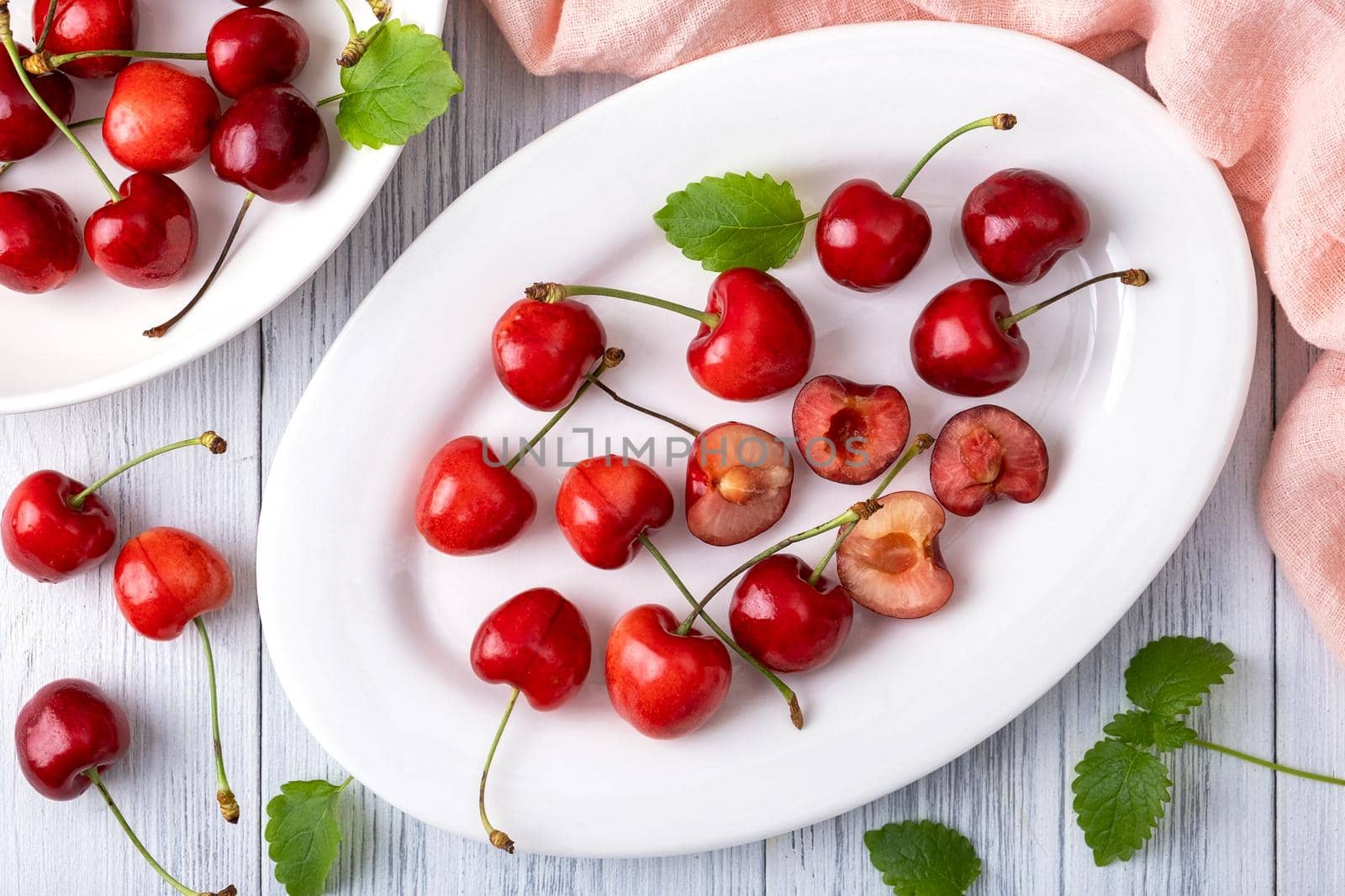 Ripe juicy sweet cherry lies on a white porcelain plate on a light wooden surface. Summer healthy food. Selective focus. View from above.